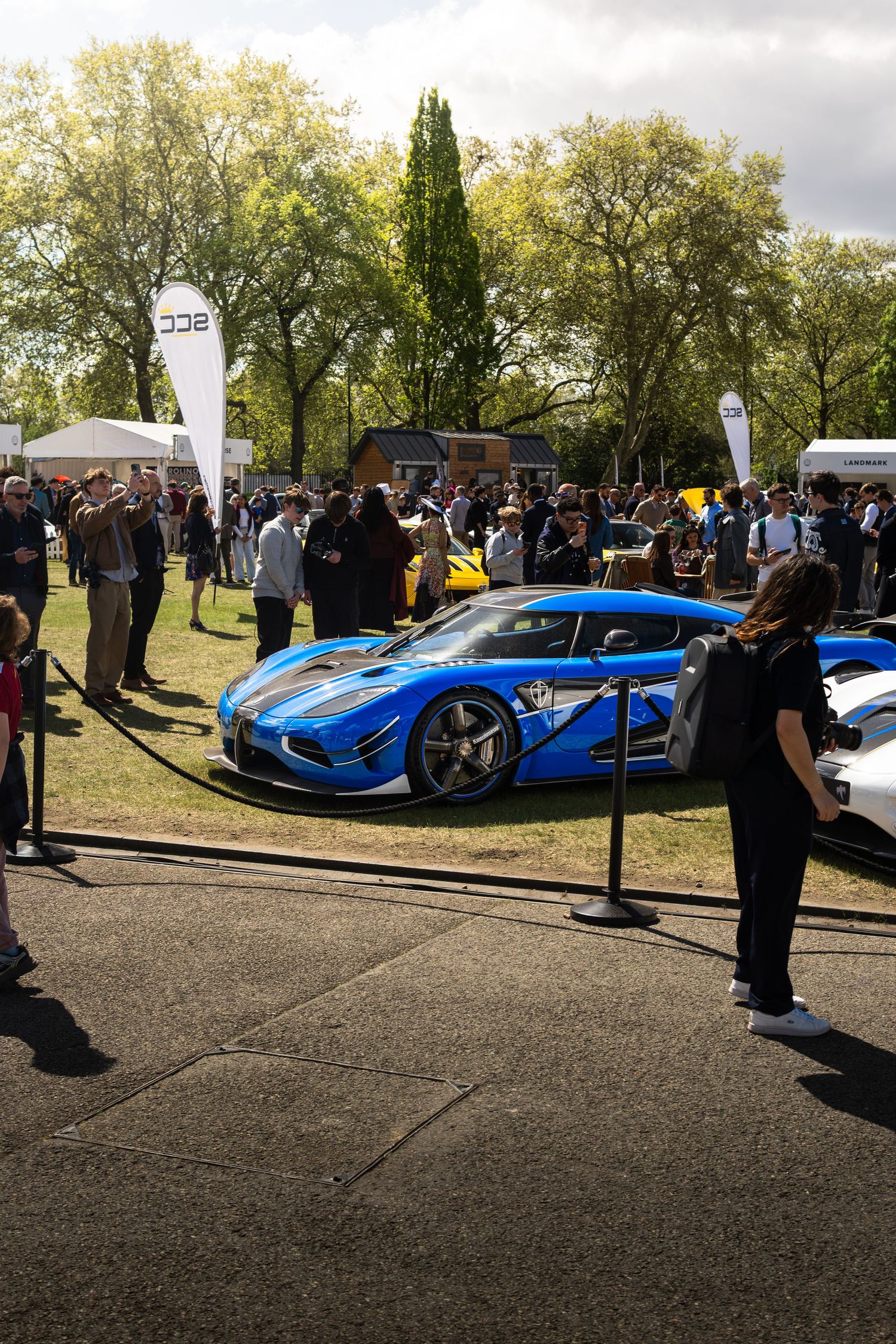 Blue Koenigsegg Regera supercar on display at an outdoor exotic car show with large crowd.