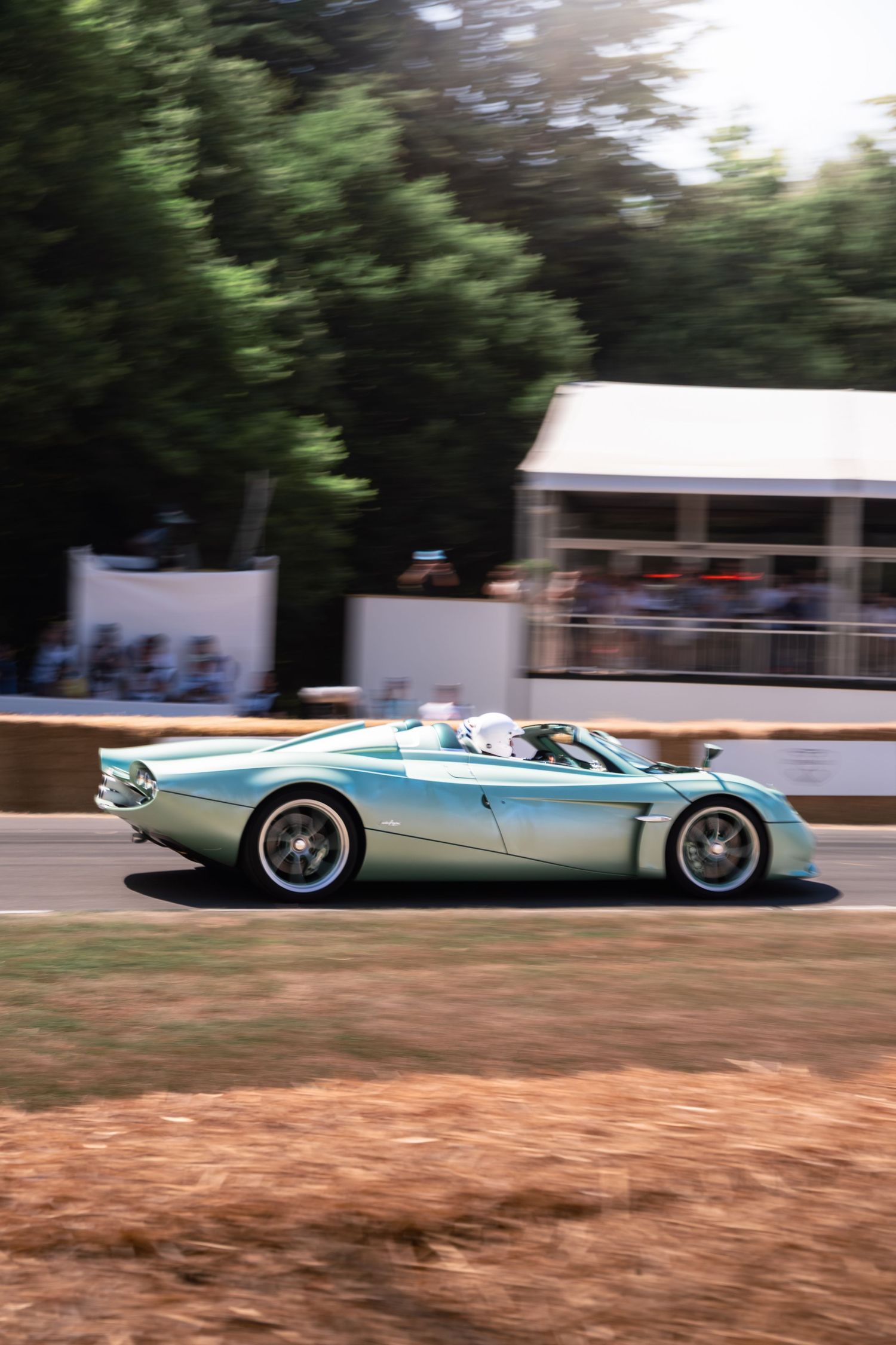 A sleek mint green convertible supercar speeds along a race track at Goodwood Festival of Speed.