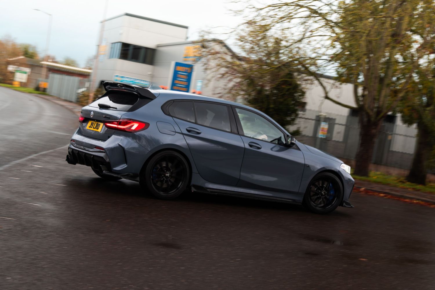 Grey BMW 1 Series M Sport hatchback cornering on wet tarmac road.