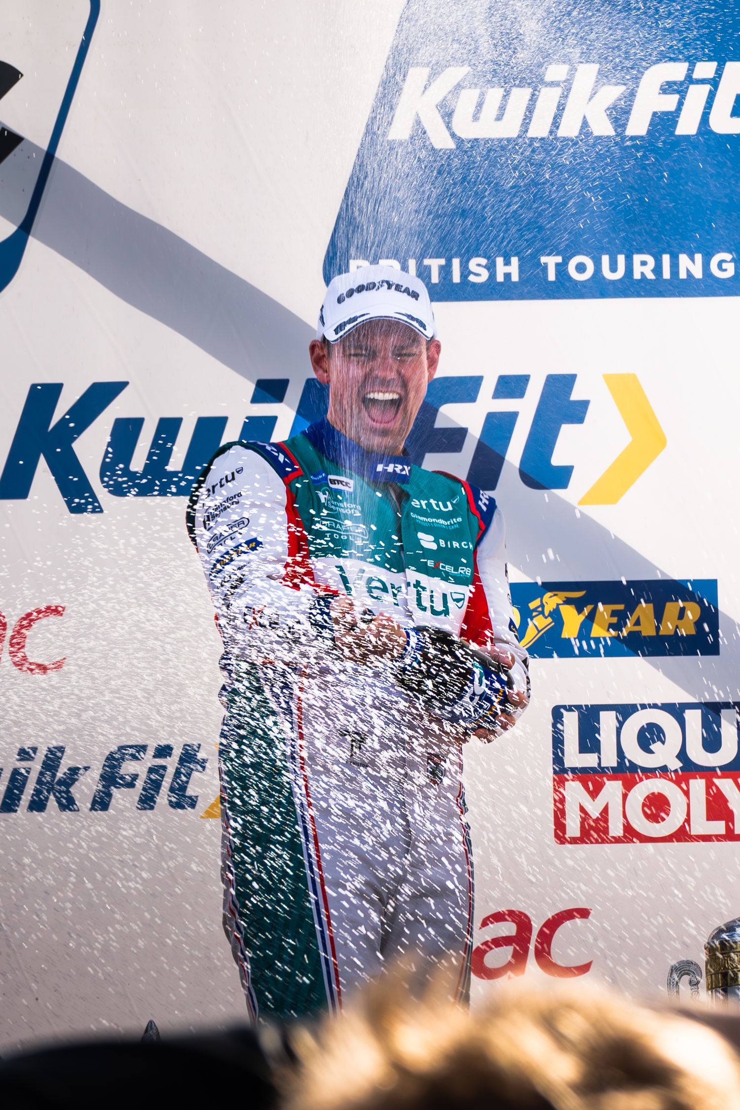 A racing driver celebrates with champagne spray on the KwikFit British Touring Car Championship podium.