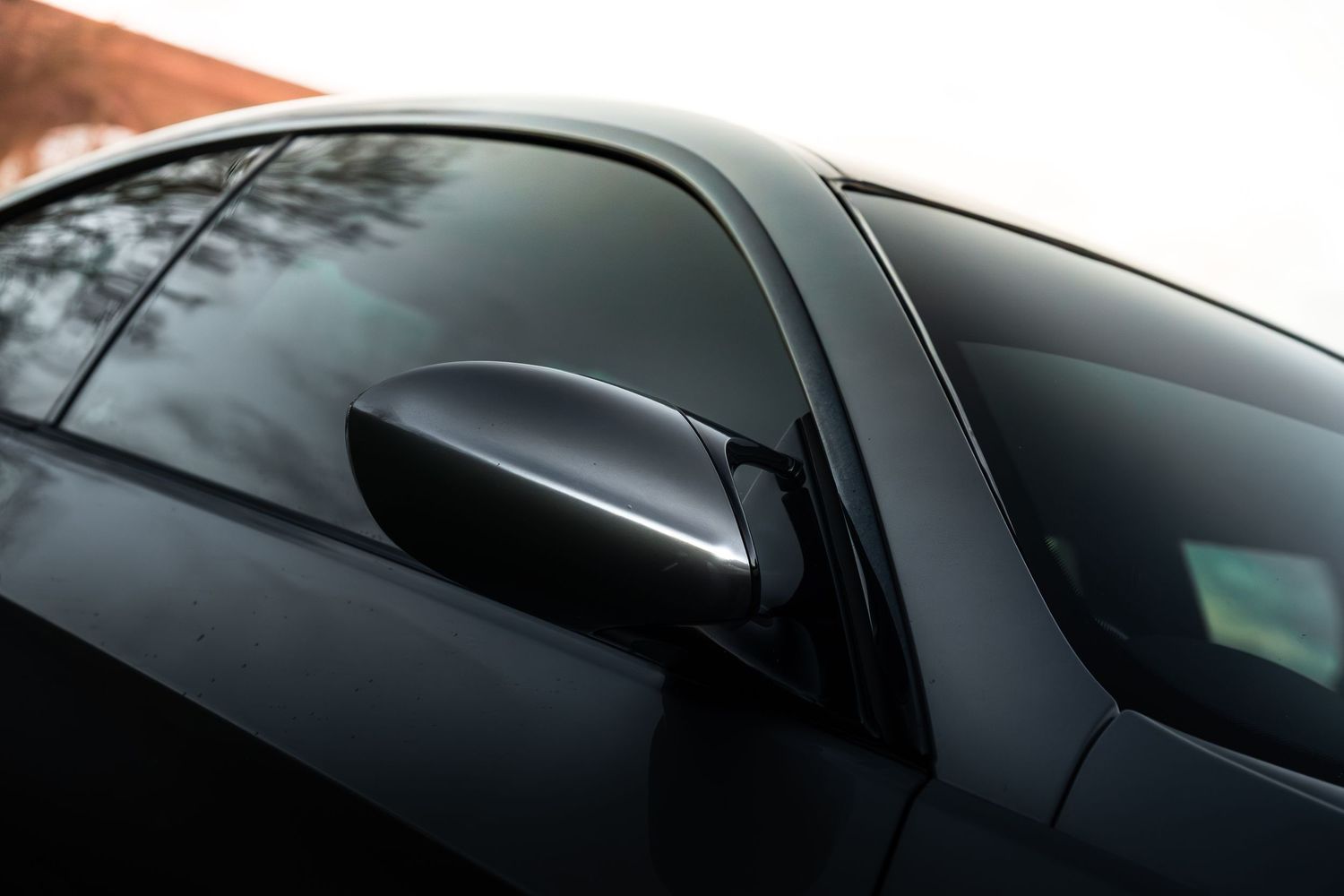 Close-up detail of BMW M3 carbon fibre side mirror and tinted window glass.