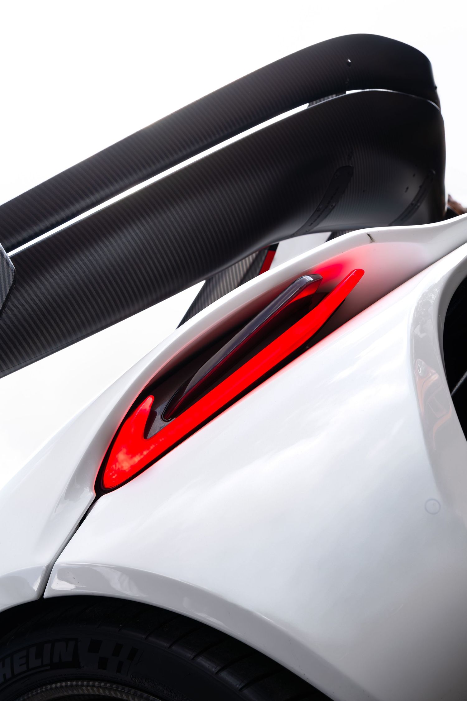 Close-up of white supercar rear with carbon fiber wing and red tail light detail.