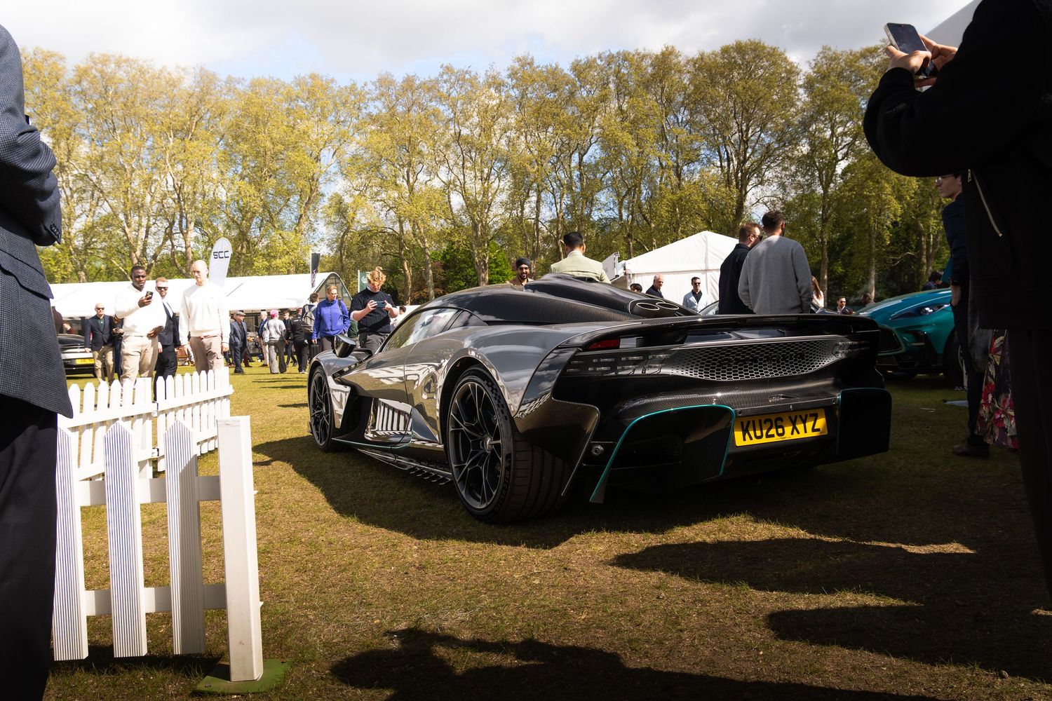 Rear view of a silver Aston Martin Vulcan supercar displayed at an outdoor luxury car show event.