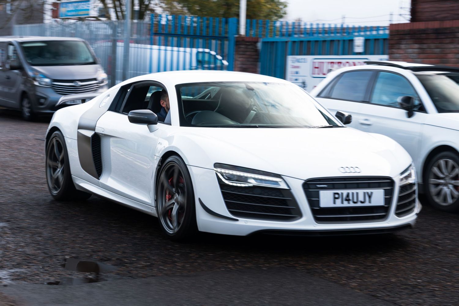 White Audi R8 V10 with red brake calipers and plate P14UJY driving through UK industrial estate.