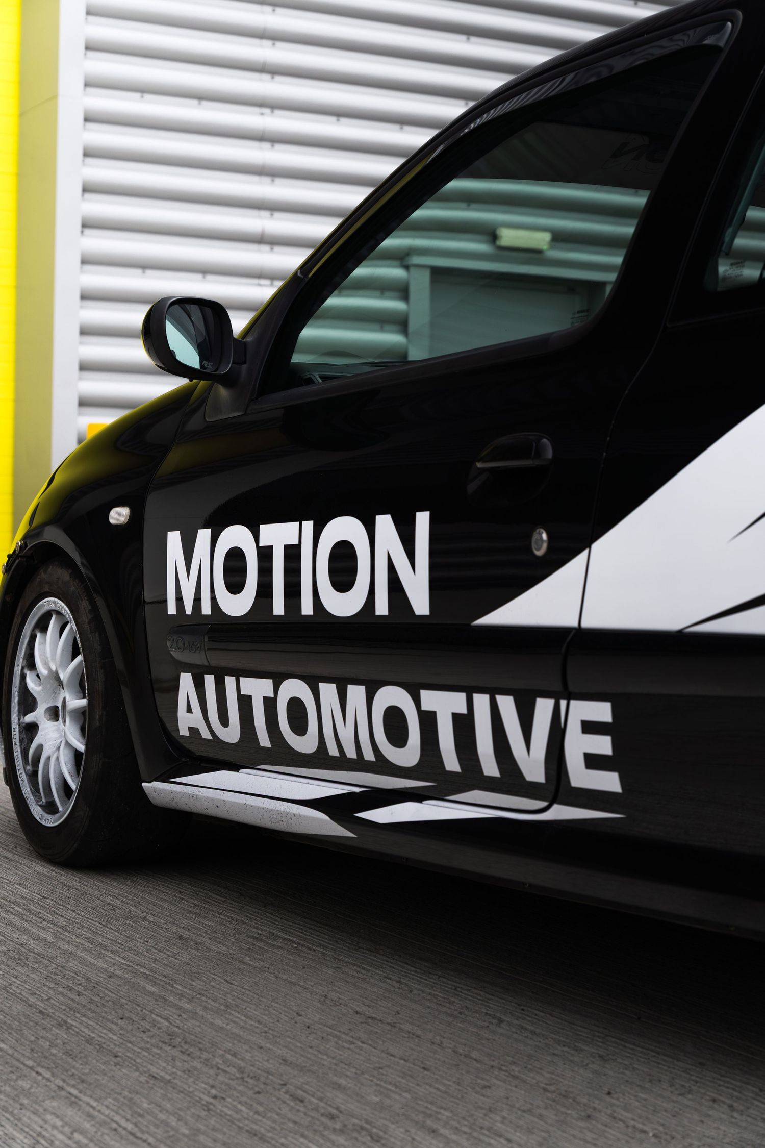 Side door detail of a black Renault Clio featuring Motion Automotive branding against a yellow garage door.