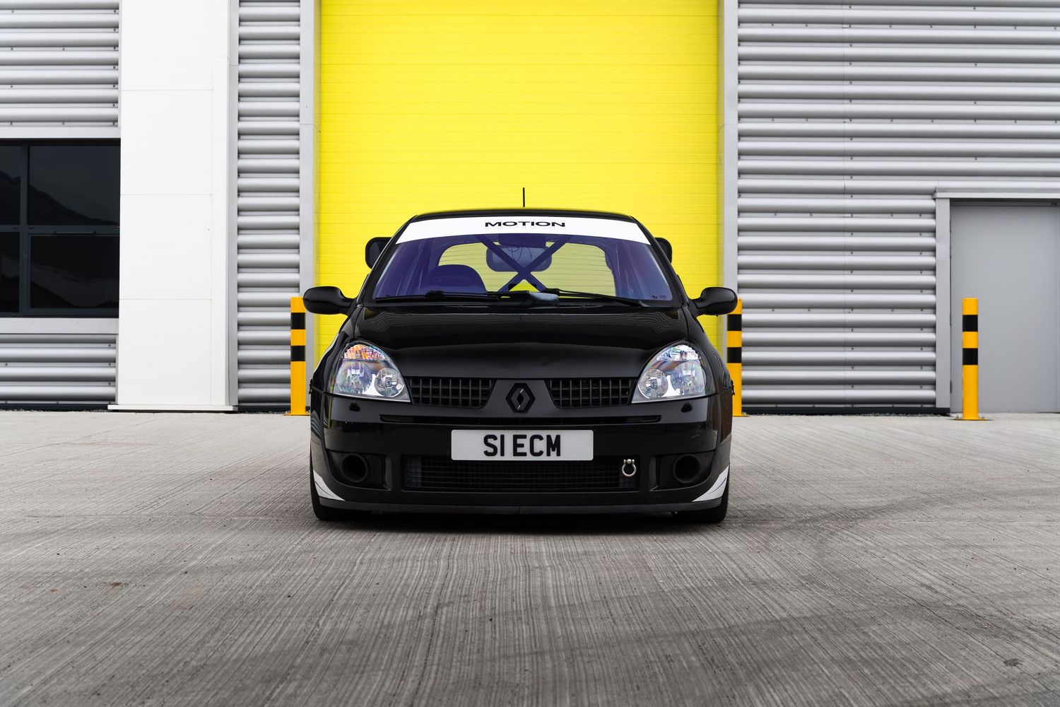 Front view of a black Renault Clio with Motion branding parked in front of yellow garage doors.