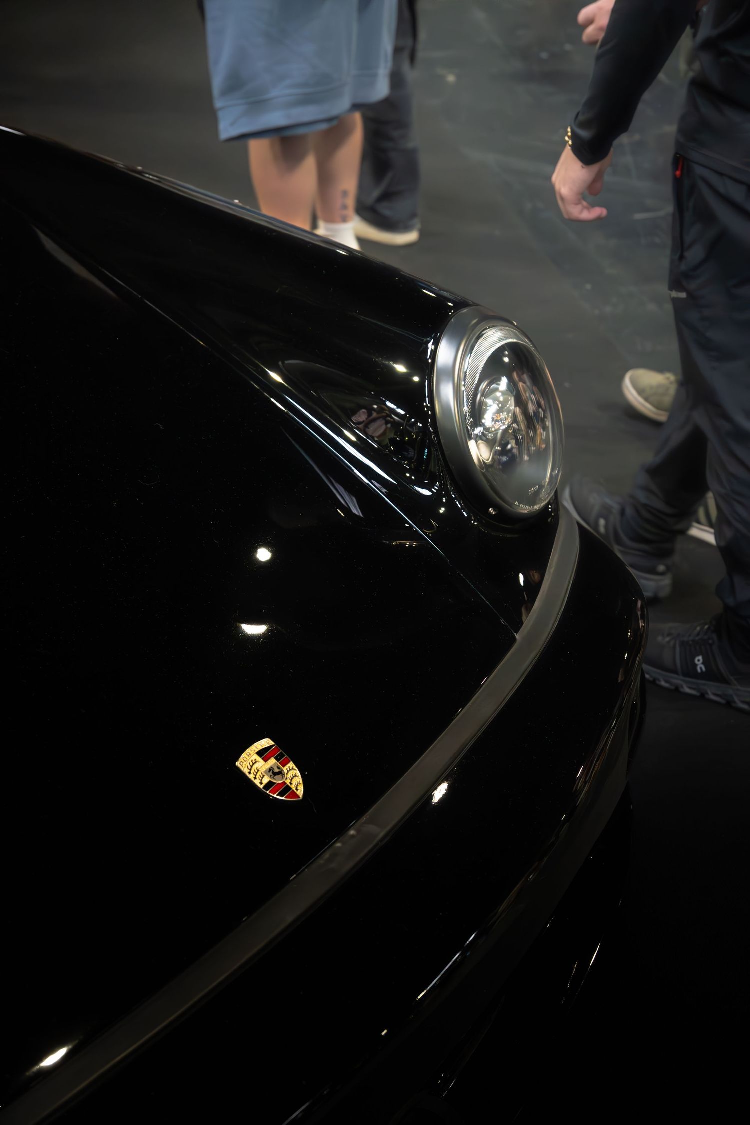 Close-up of a black Porsche front hood showing iconic Porsche crest badge and round headlight.