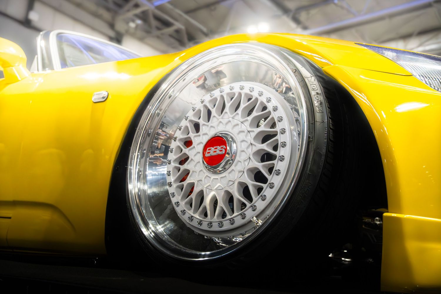 Close-up of a polished BBS mesh alloy wheel on a yellow sports car at an auto show.
