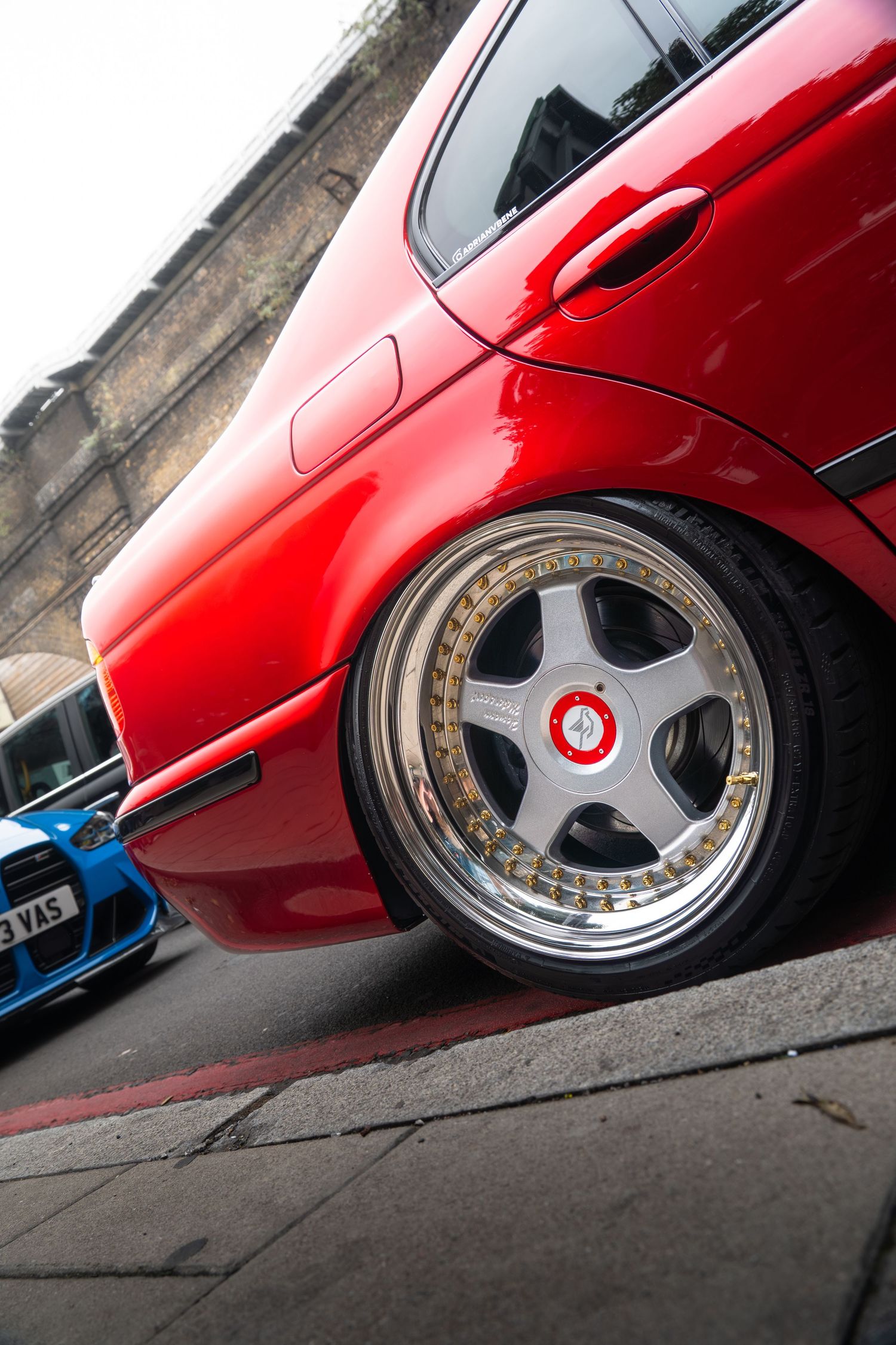 Low-angle view of a red BMW on deep-dish aftermarket wheels at a car meet.
