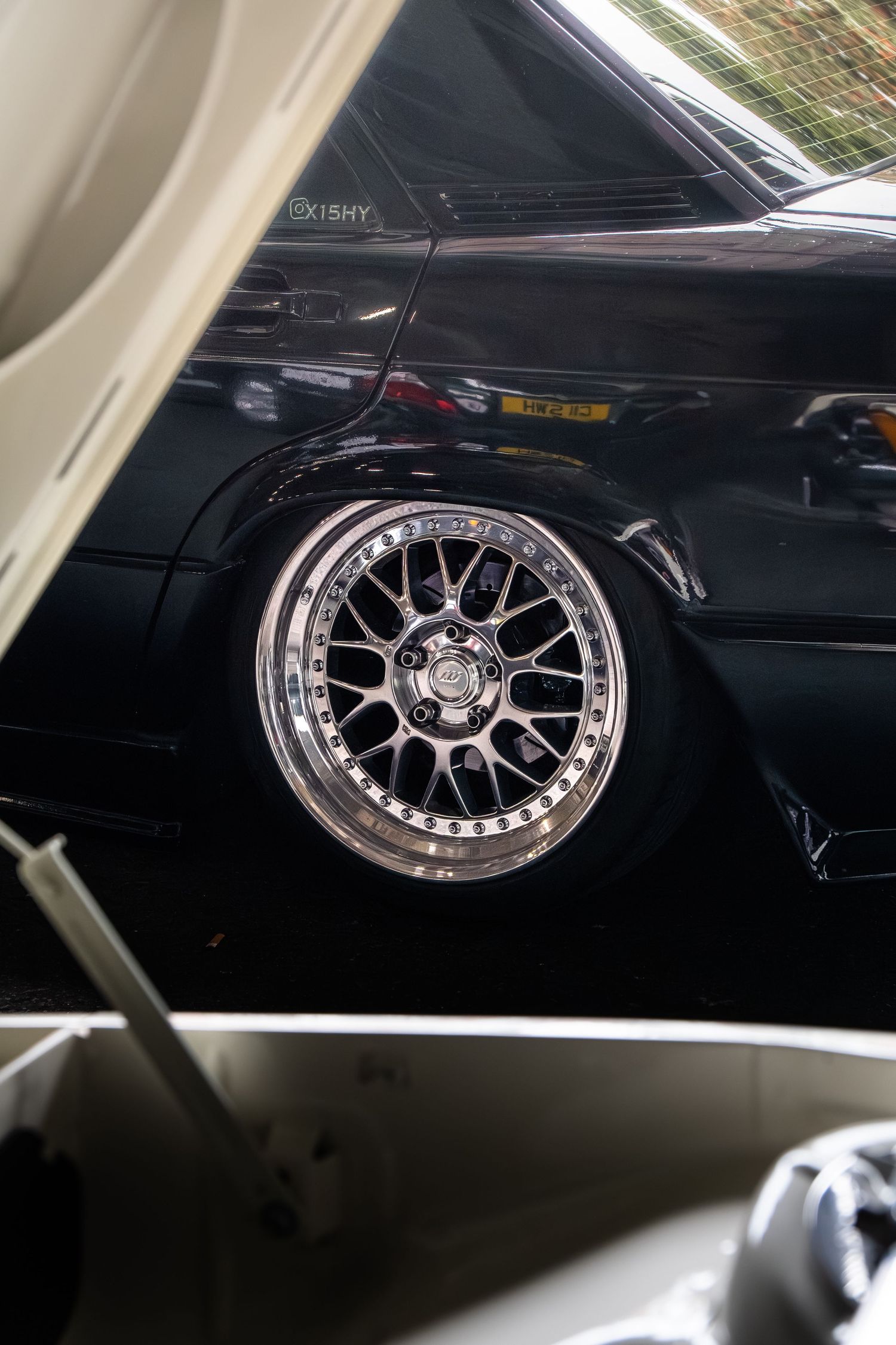 Close-up of a polished multi-spoke aftermarket alloy wheel on a lowered black modified car.