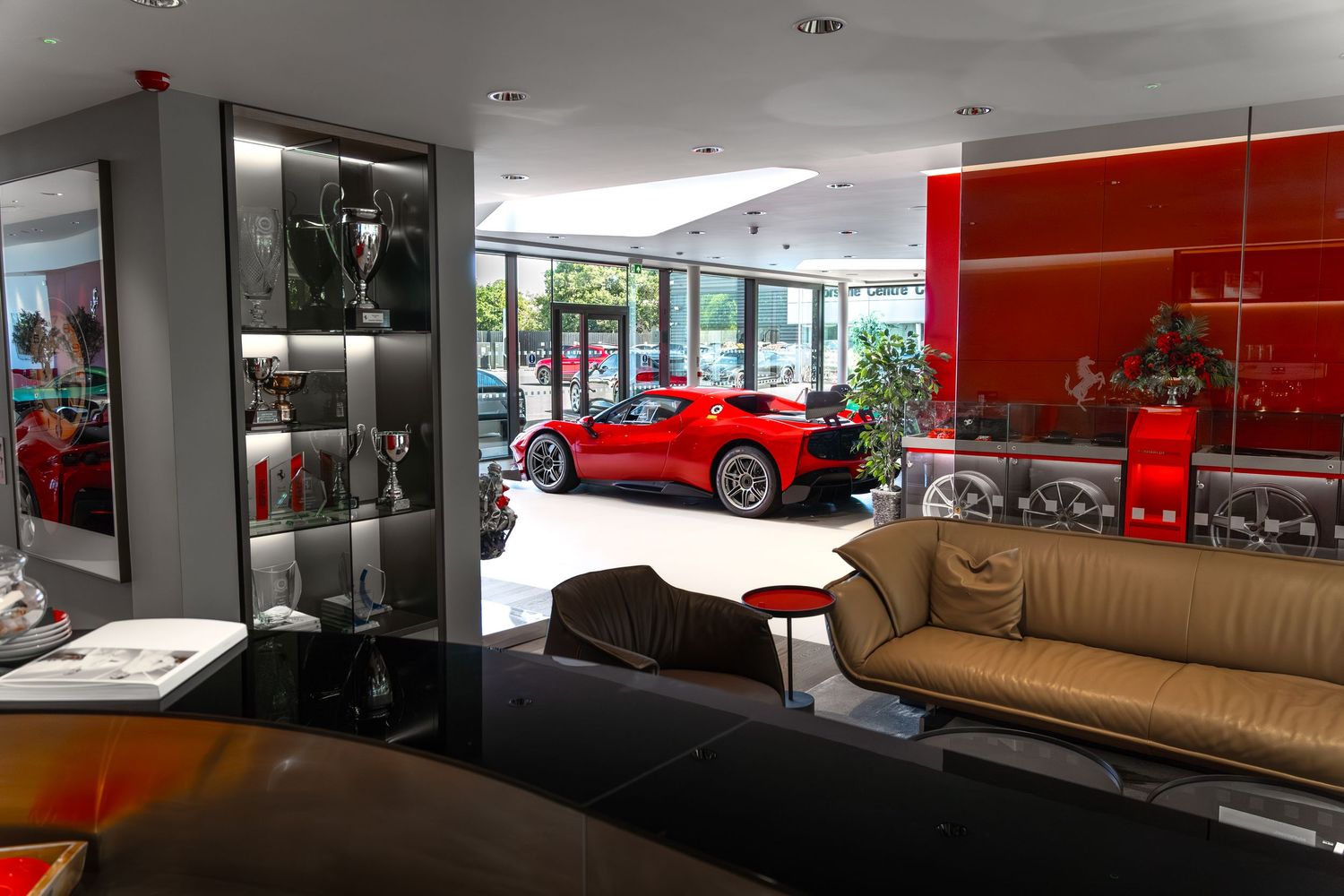 Luxury Ferrari dealership showroom featuring a red sports car, trophy display case, and elegant leather sofa.