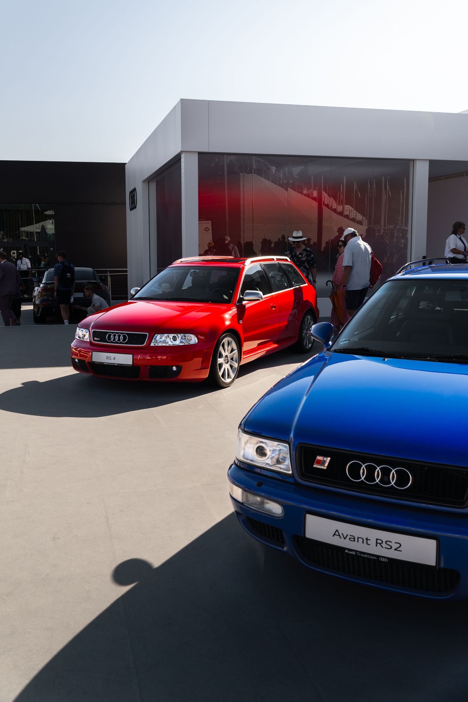 Two Audi RS cars, a red RS4 Avant and blue RS2 Avant, displayed at an outdoor automotive event.
