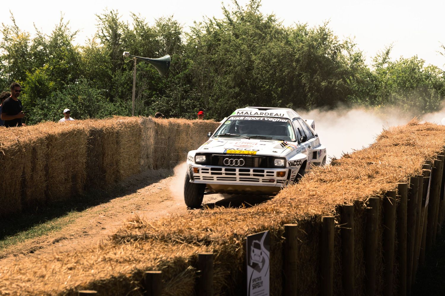 An Audi rally car kicks up dust on a dirt track course during a competitive off-road racing event.
