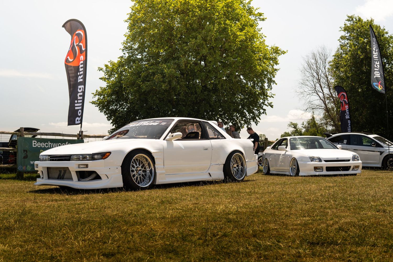Two white modified Nissan Silvia S14 cars parked at a car show with branded banners.