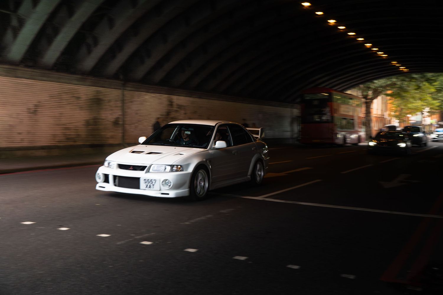 White Mitsubishi Lancer Evolution with body kit driving under a bridge at night.