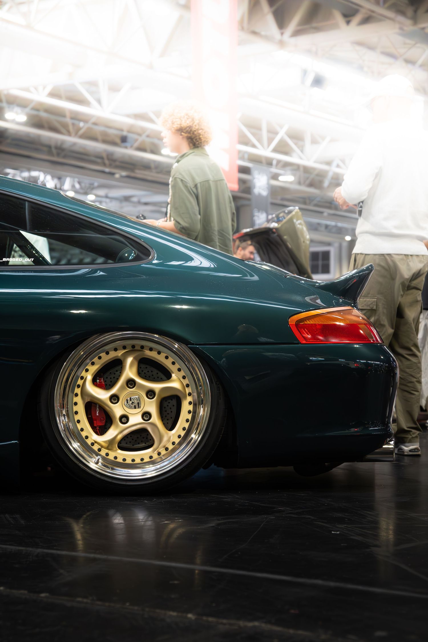 Dark green modified car with gold multi-spoke alloy wheels on display at an auto show.
