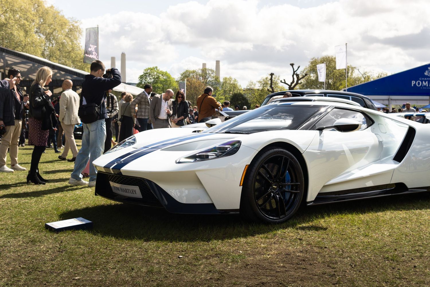 White Ford GT supercar with blue stripes on display at an outdoor Pommery sponsored car show.