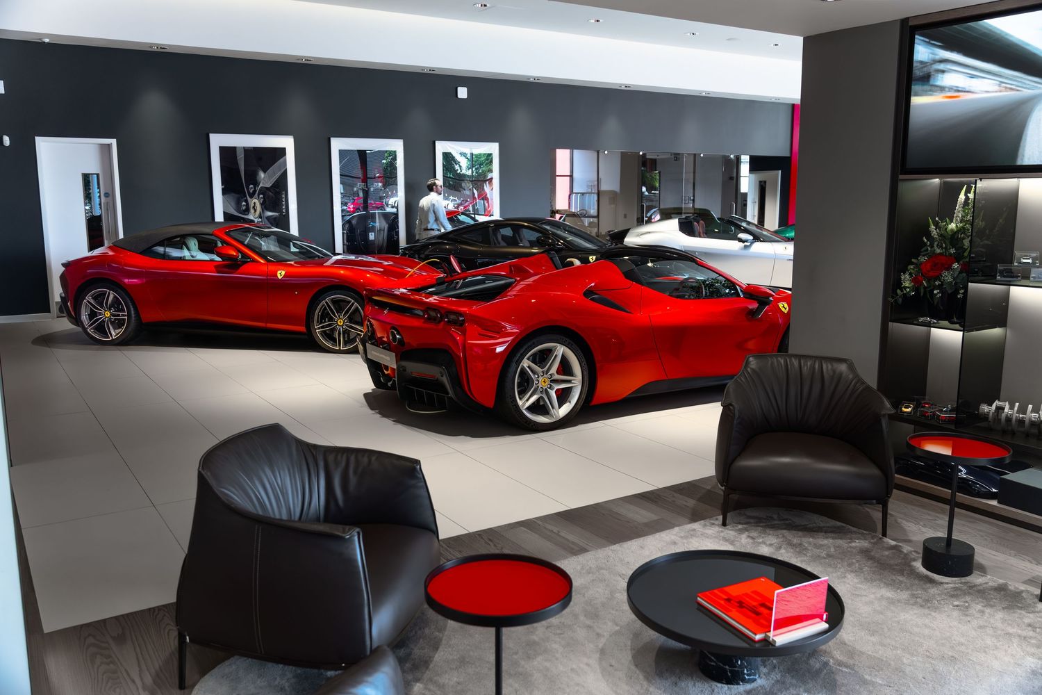 Luxury Ferrari dealership showroom featuring red sports cars on display with black leather seating and modern interior design.