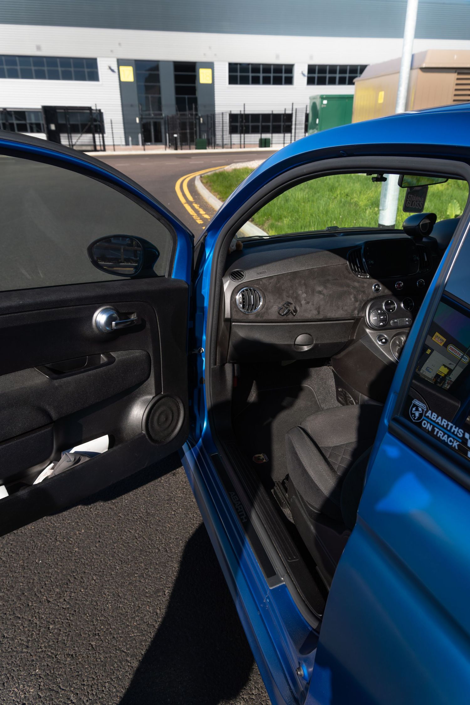 Interior view of a blue Abarth 500 with open door showing dark grey upholstery and dashboard details.
