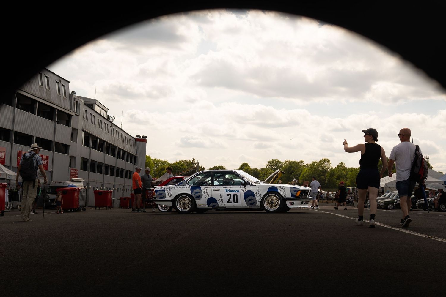 Classic white BMW racing car number 28 in a pit lane viewed through a circular tunnel opening.