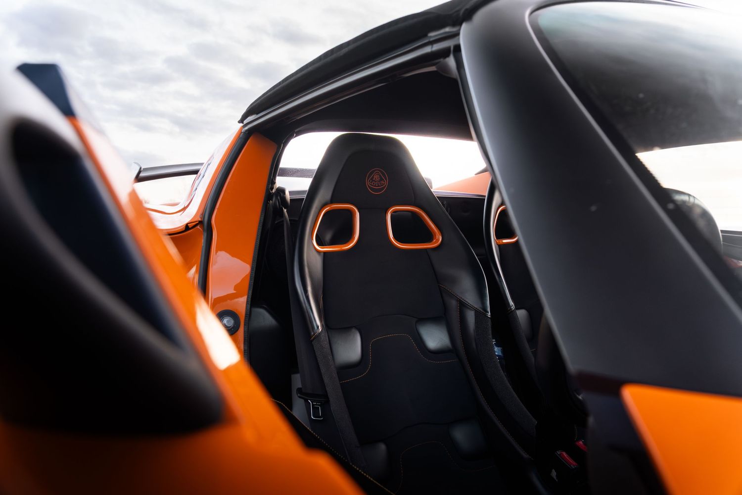 Interior view of orange Lotus Elise showing black bucket seats with orange trim details.