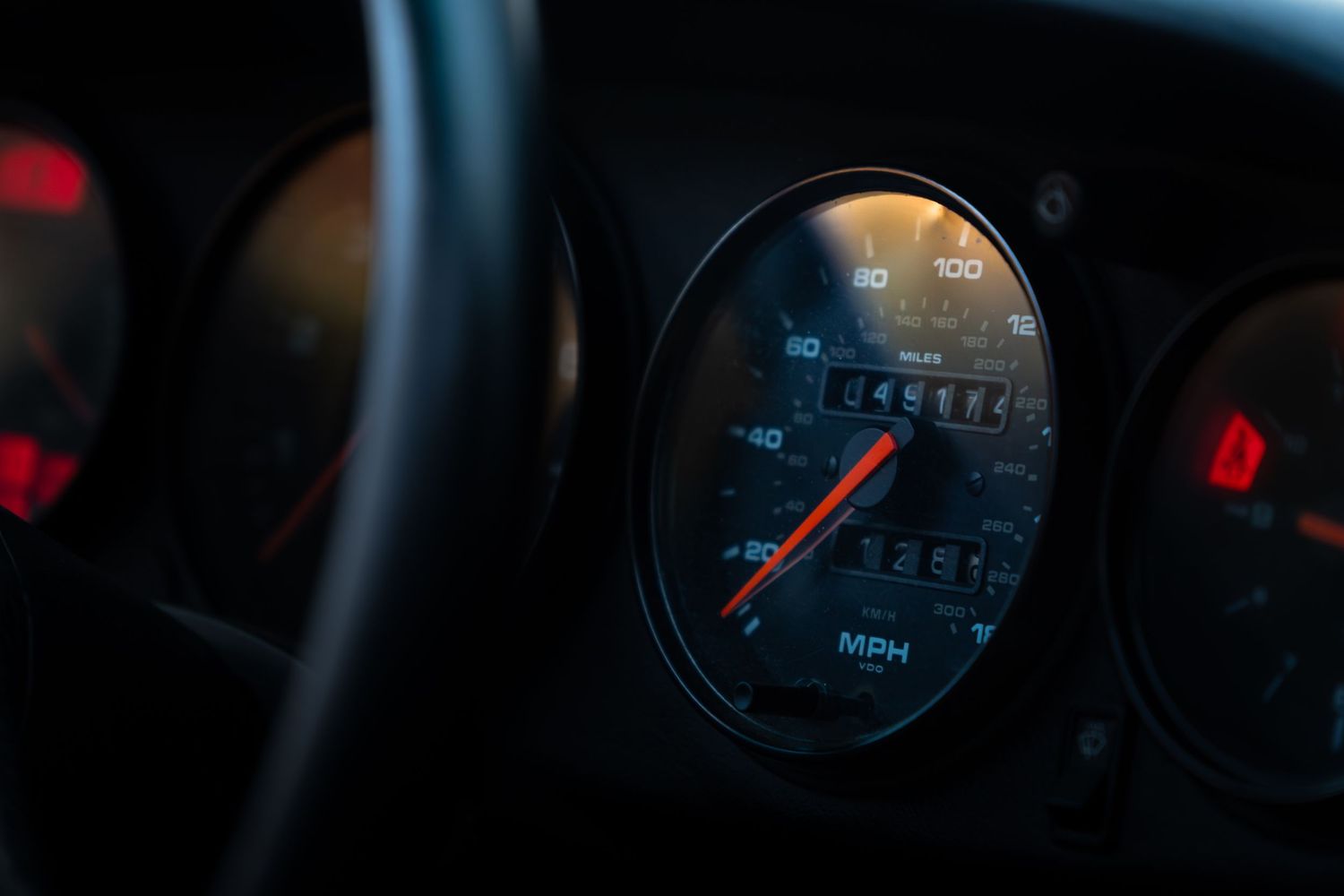 Close-up of a Porsche 911 speedometer showing 45,187 miles on the odometer in a dark dashboard interior.