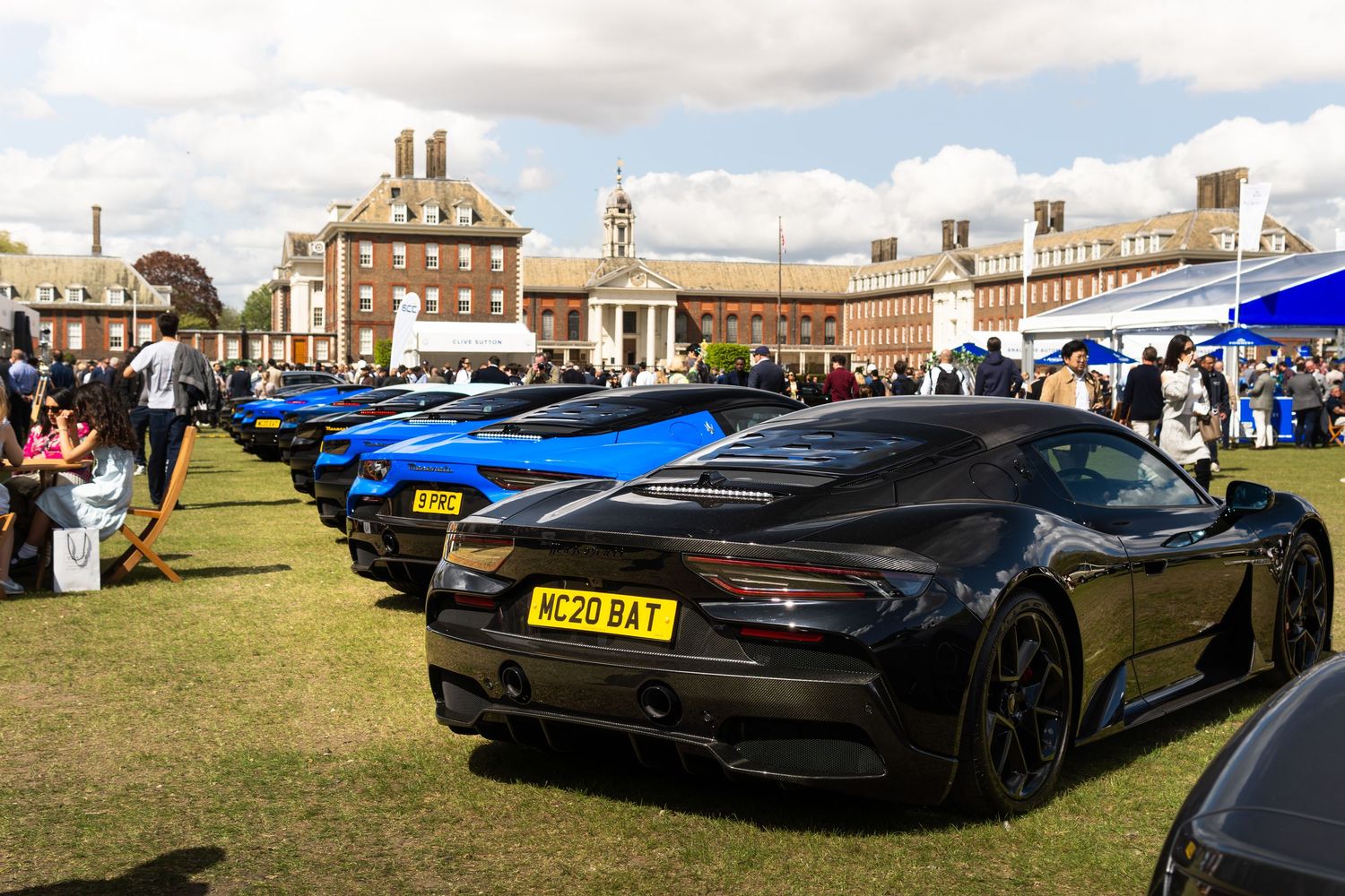 Black Aston Martin DBS supercar with yellow license plate at a prestigious outdoor concours event.