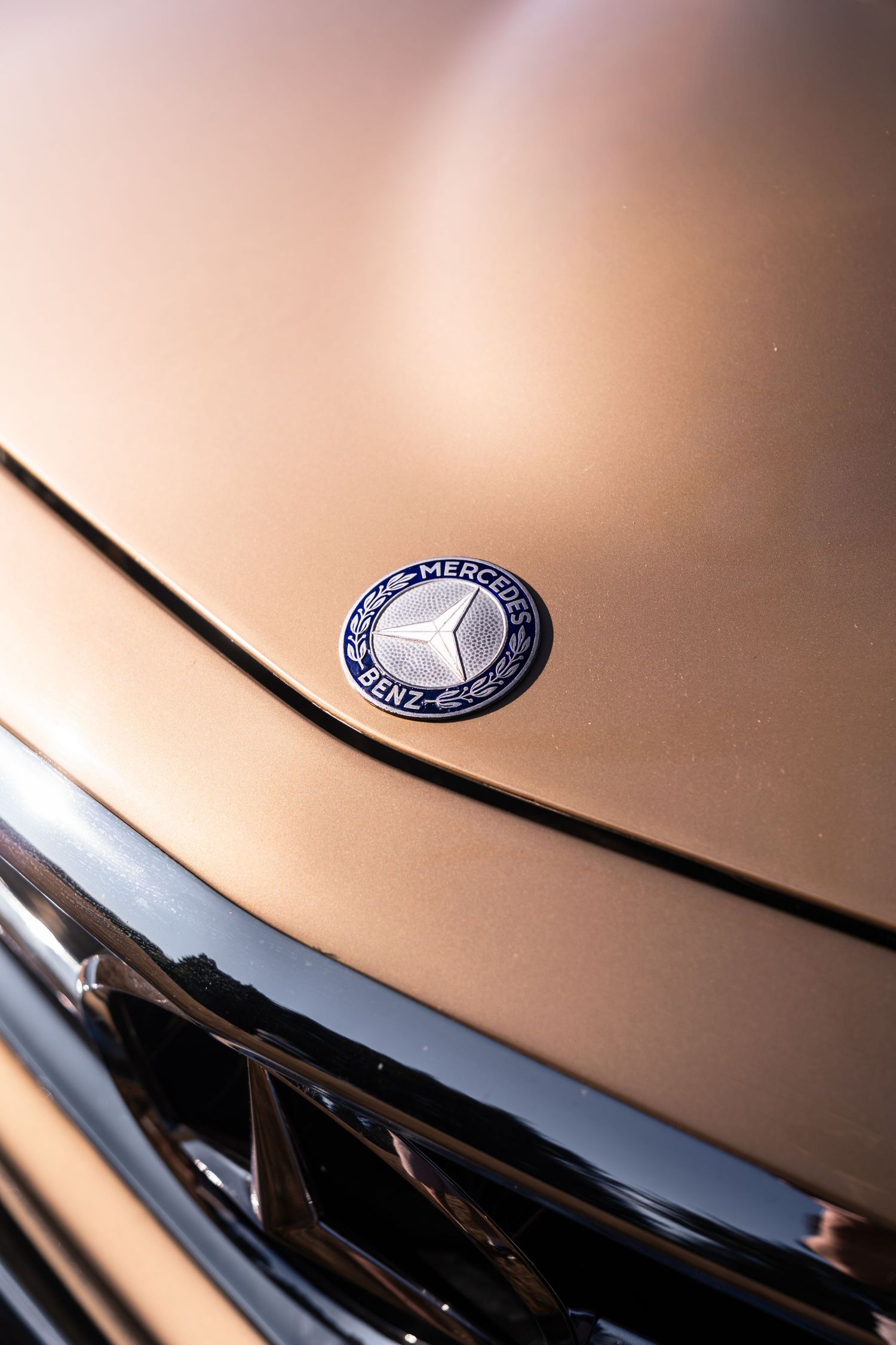 Close-up of a Mercedes-Benz hood emblem on a gold luxury car, showcasing the iconic three-pointed star logo.