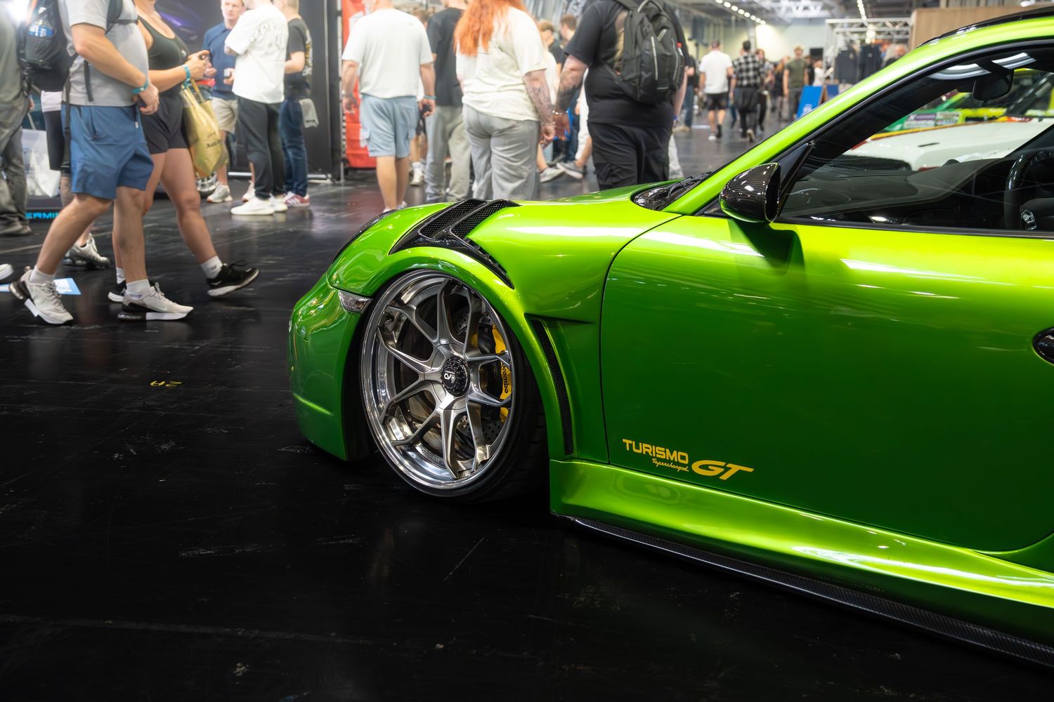 Lime green Porsche 911 Turbo GT with wide body kit and chrome wheels on display at a car show.