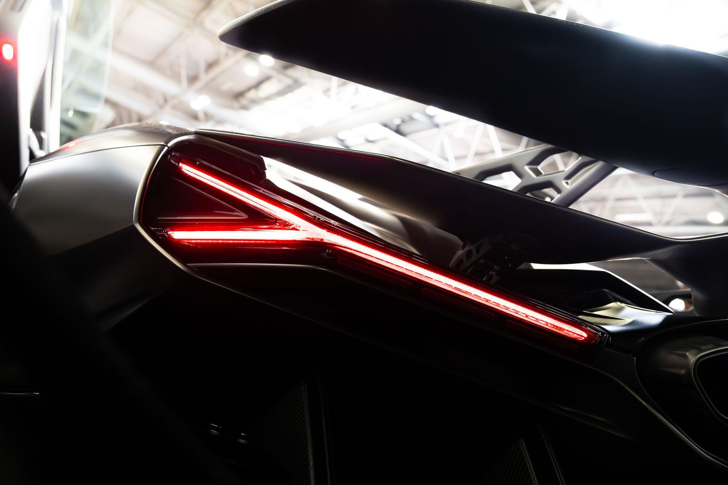 Close-up of sleek black car bodywork featuring illuminated red LED tail lights in low light.