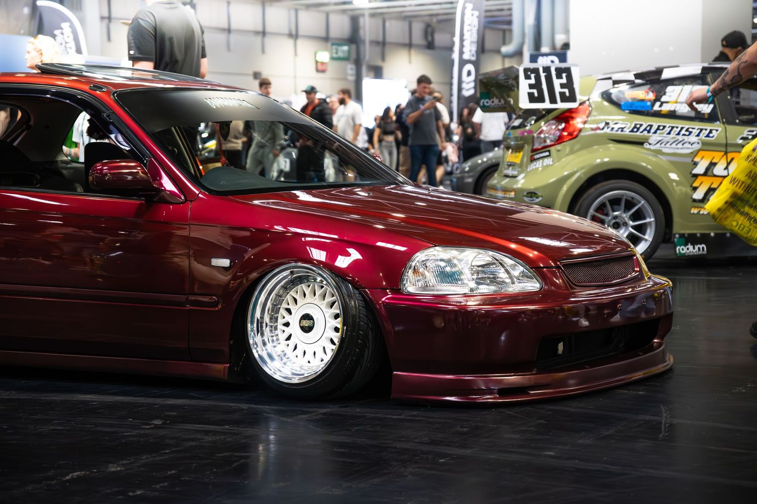 Lowered burgundy Honda Civic EK hatchback on BBS wheels at an indoor car show exhibition.