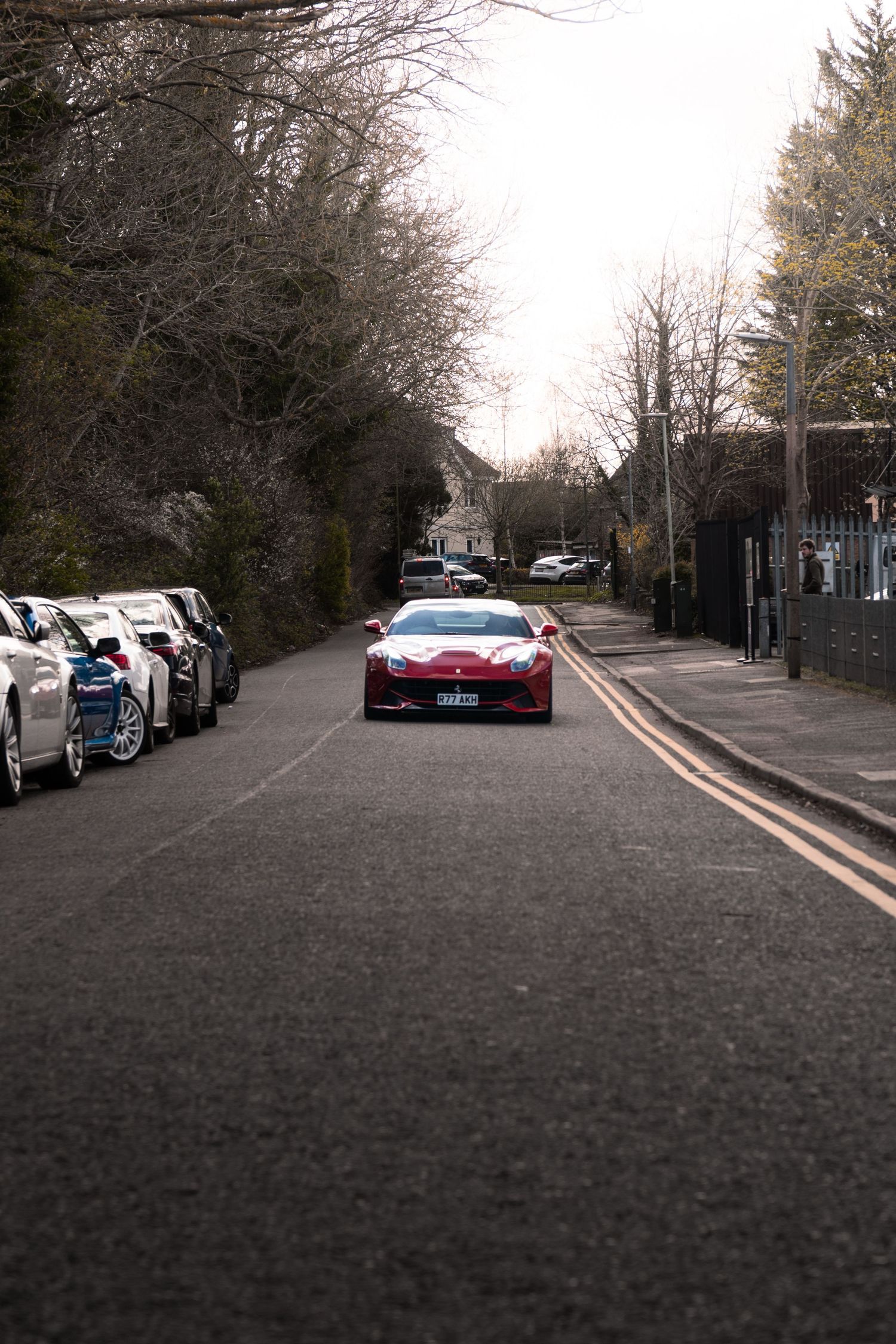 Red Aston Martin driving down a quiet residential tree-lined street.