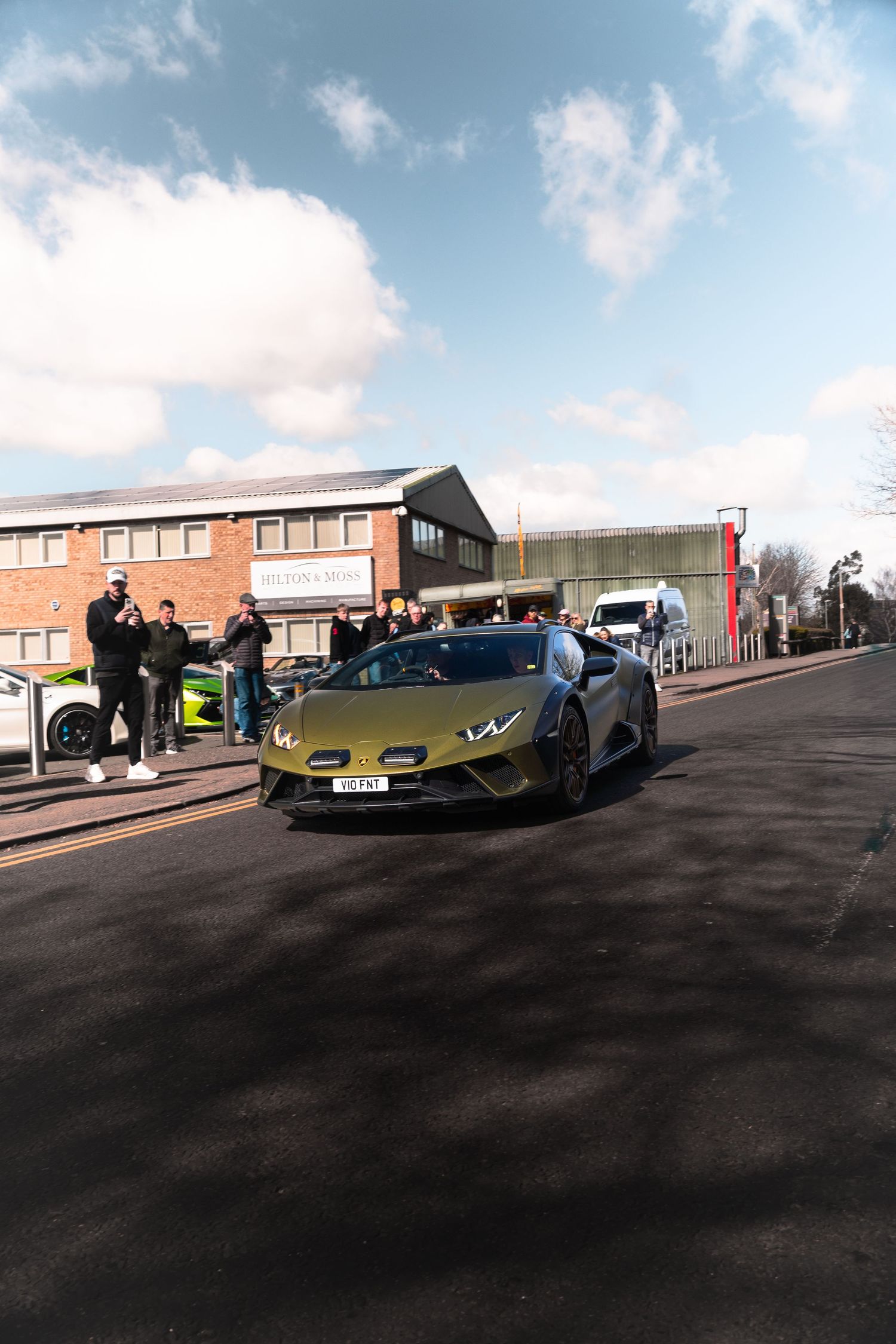 Olive green Lamborghini Huracan Performante driving on a road with spectators watching at a car meet event.