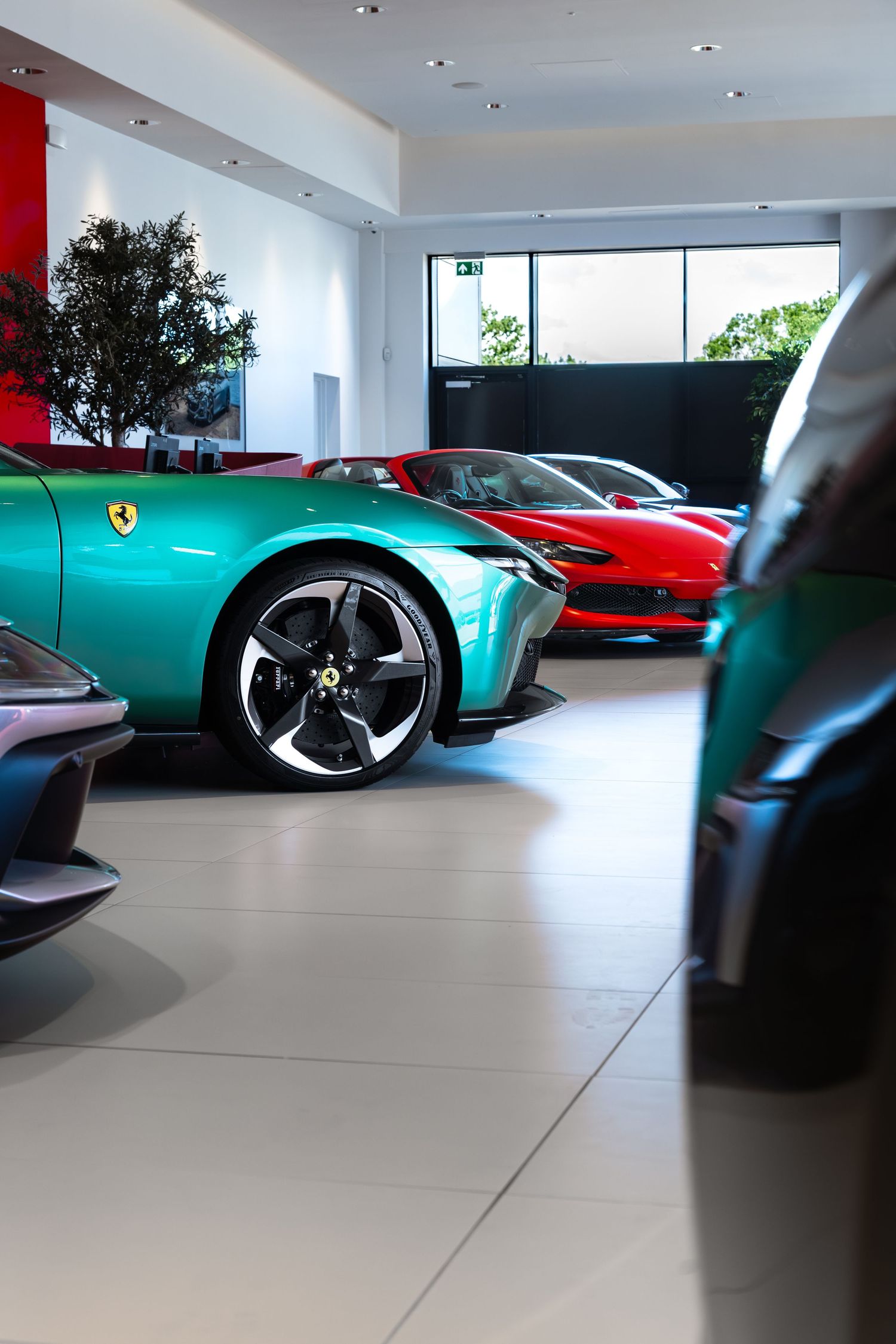 Green Ferrari sports car displayed in a luxury dealership showroom alongside red and teal Ferraris on a polished floor.