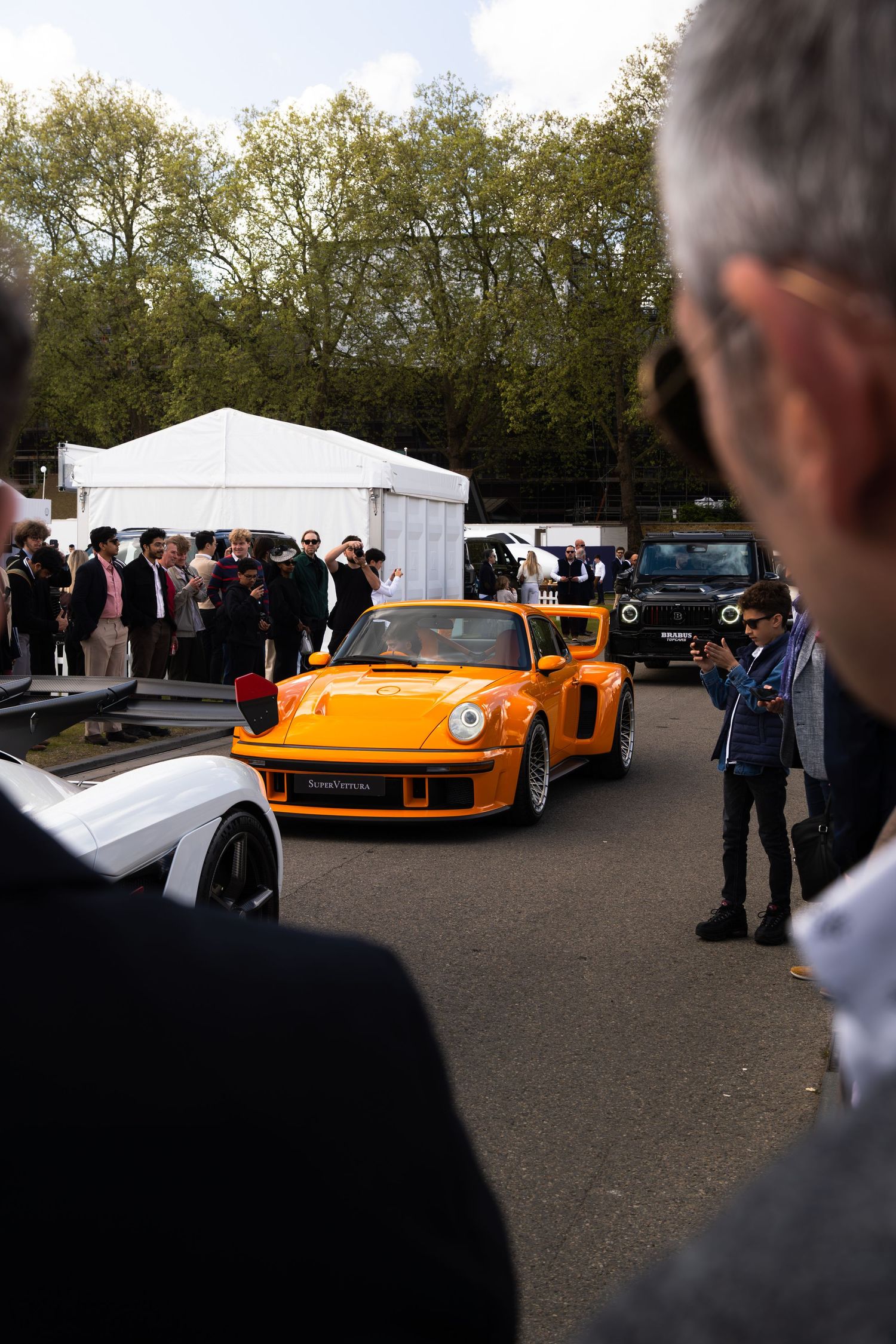 Bright orange Porsche 934 RSR on display at an outdoor automotive show with crowd watching.