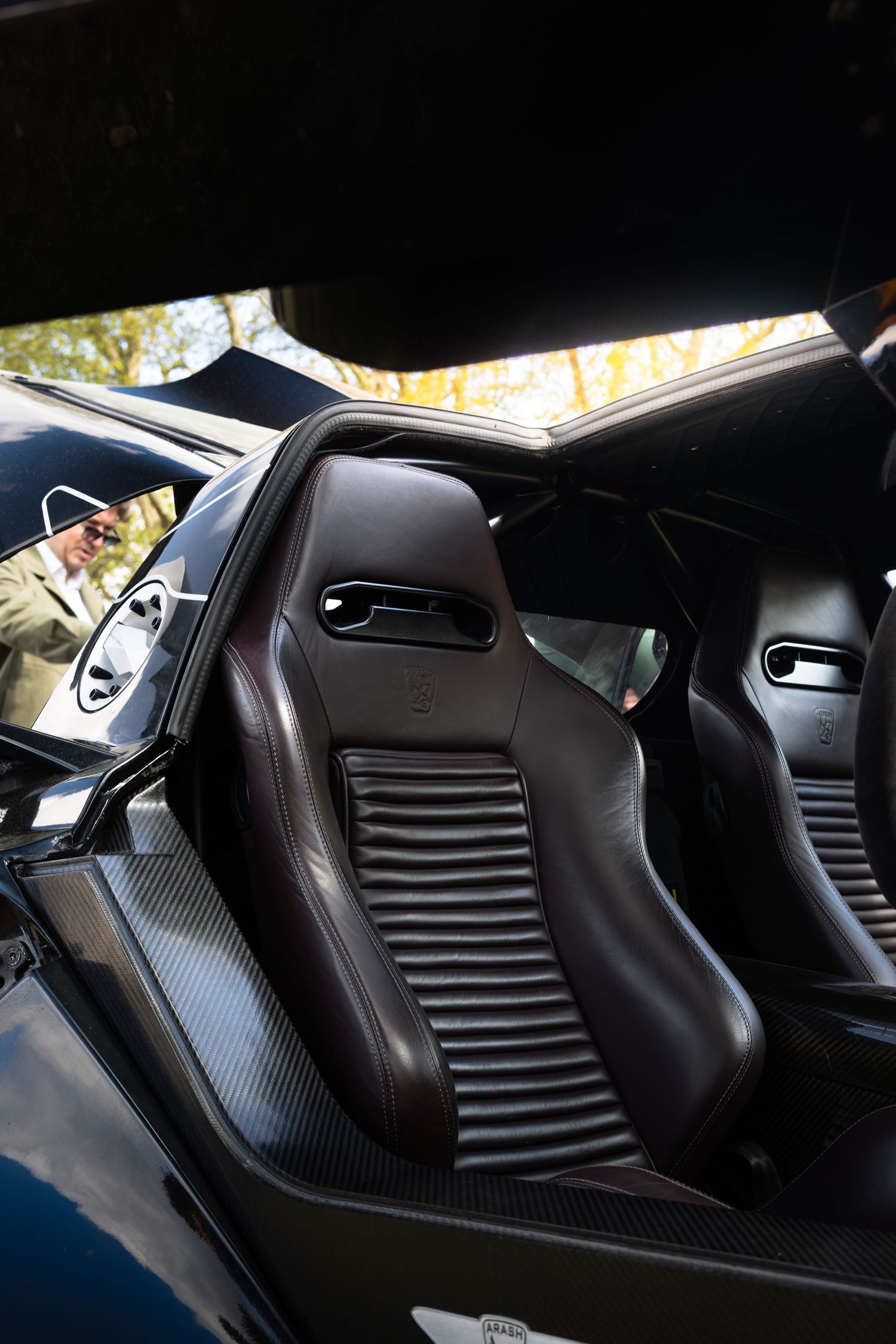 Interior view of a supercar showing dark leather bucket racing seats with carbon fiber trim and open door.