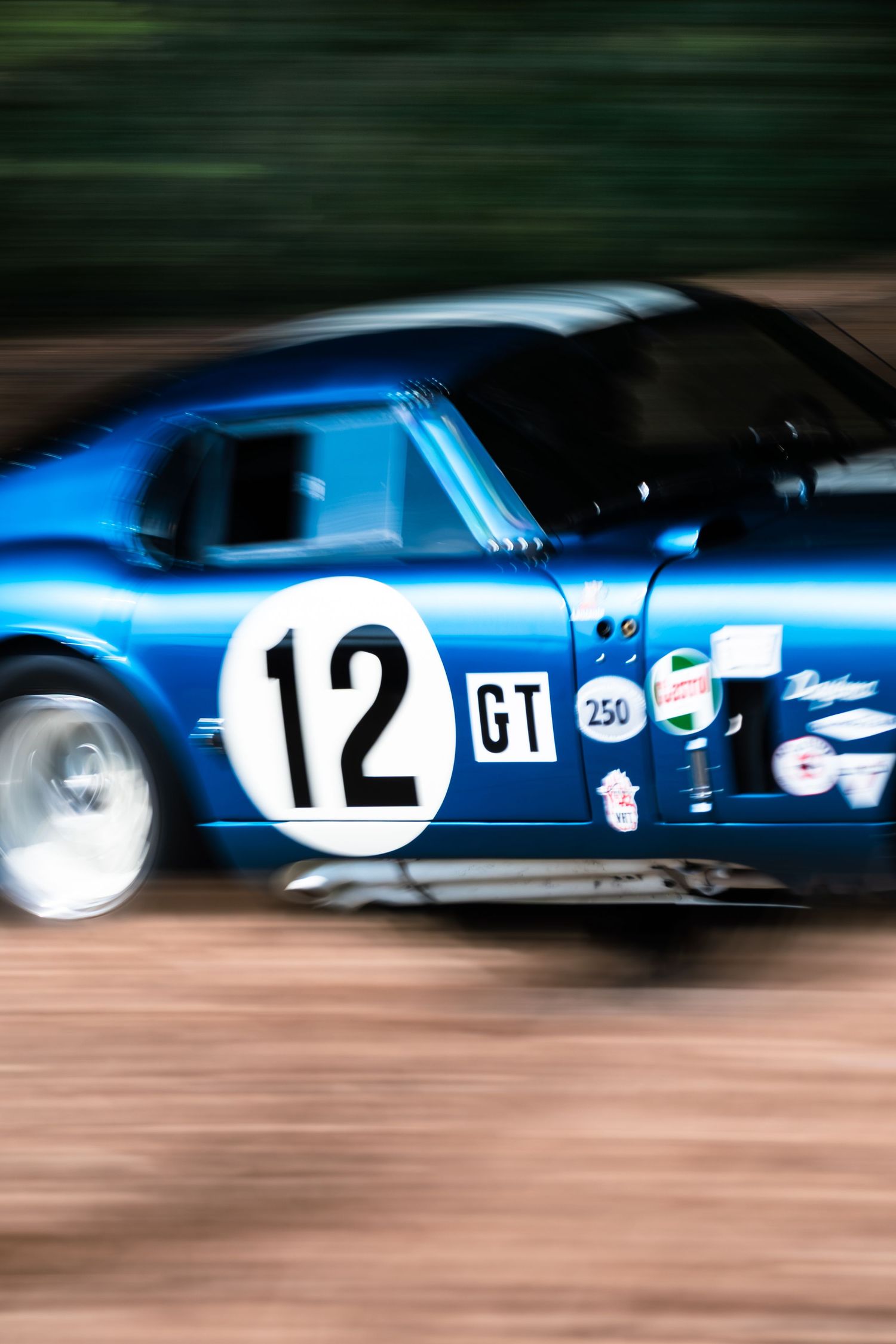 Blue GT racing car number 12 speeding on track, motion blur background capturing high-speed action at motorsport event.