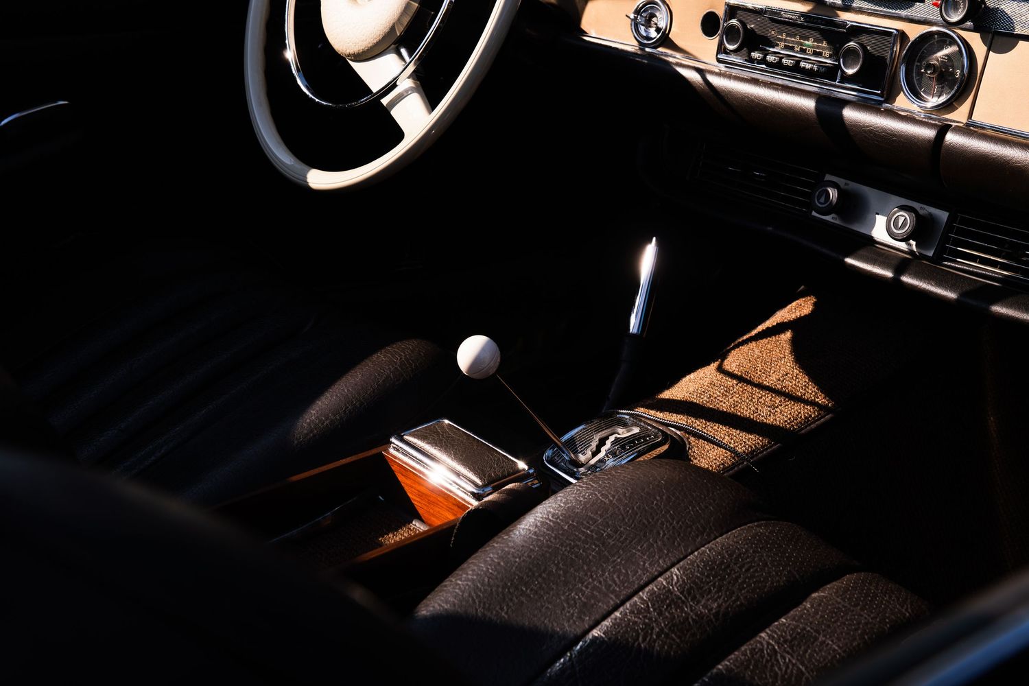 Vintage car interior with leather seats, gear shift, steering wheel, and classic dashboard in dramatic lighting.