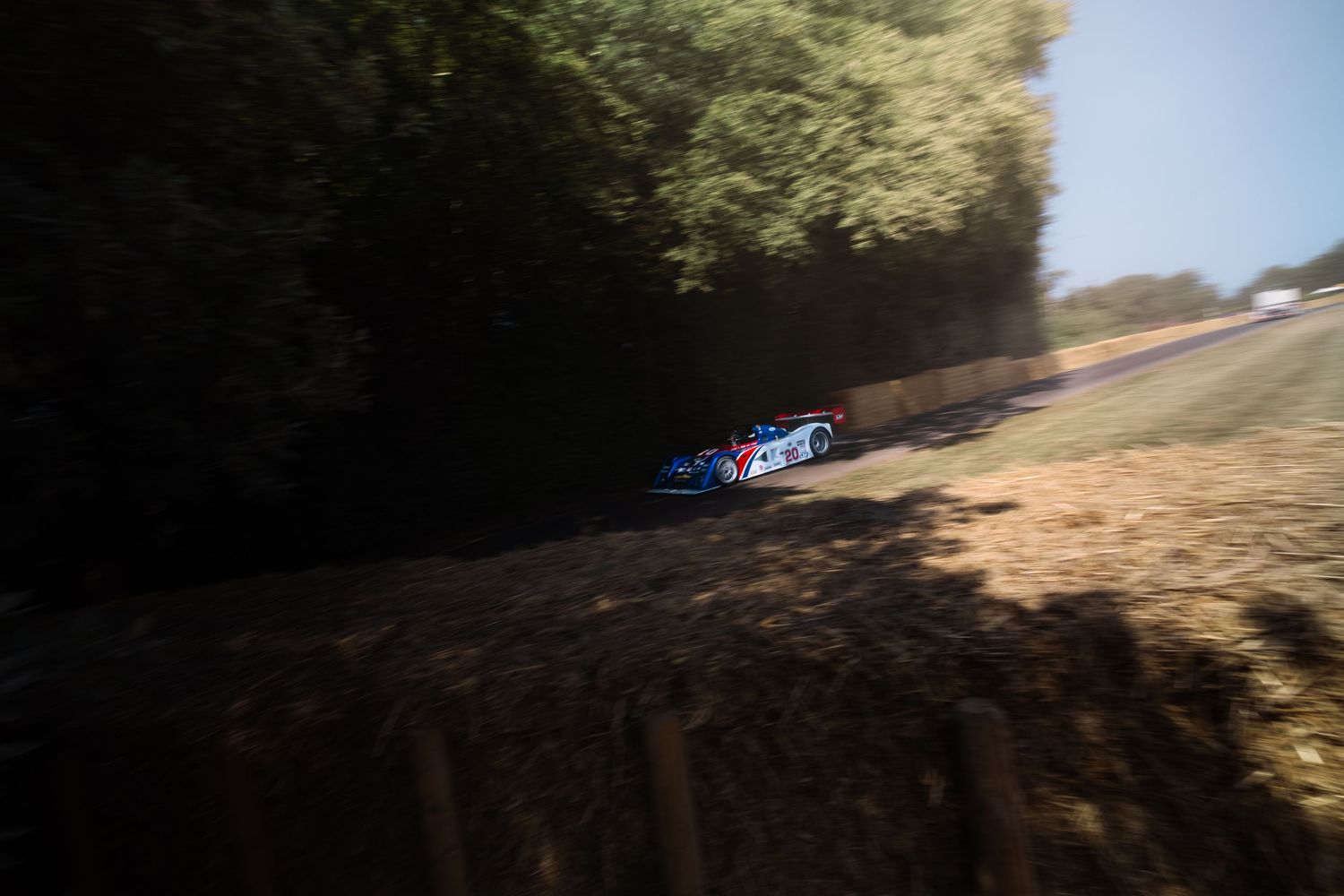 Blue racing car speeding through a tree-lined track at Goodwood Festival of Speed.