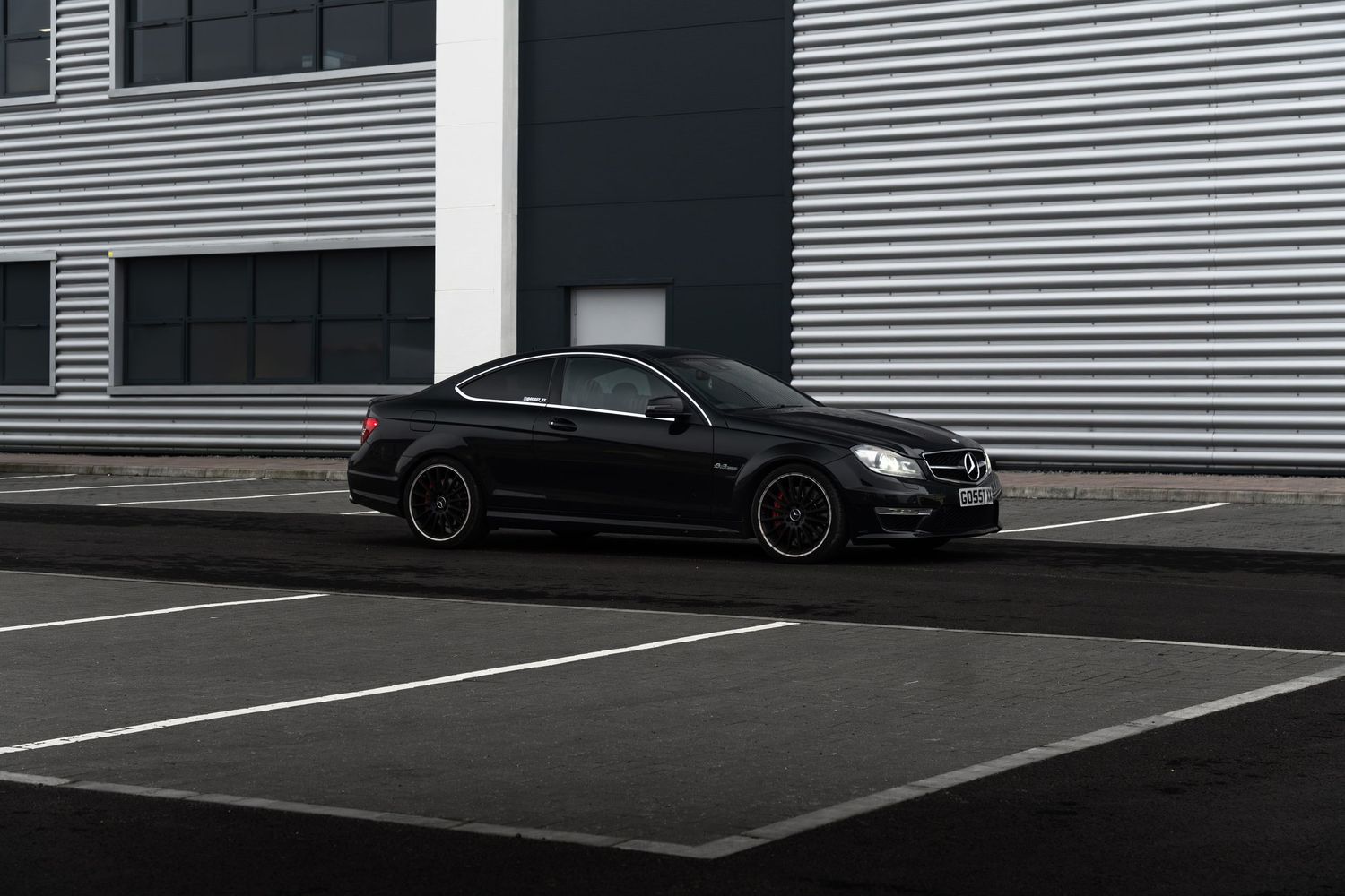 Sleek black Mercedes-AMG C63 coupe photographed against a striped industrial warehouse wall.