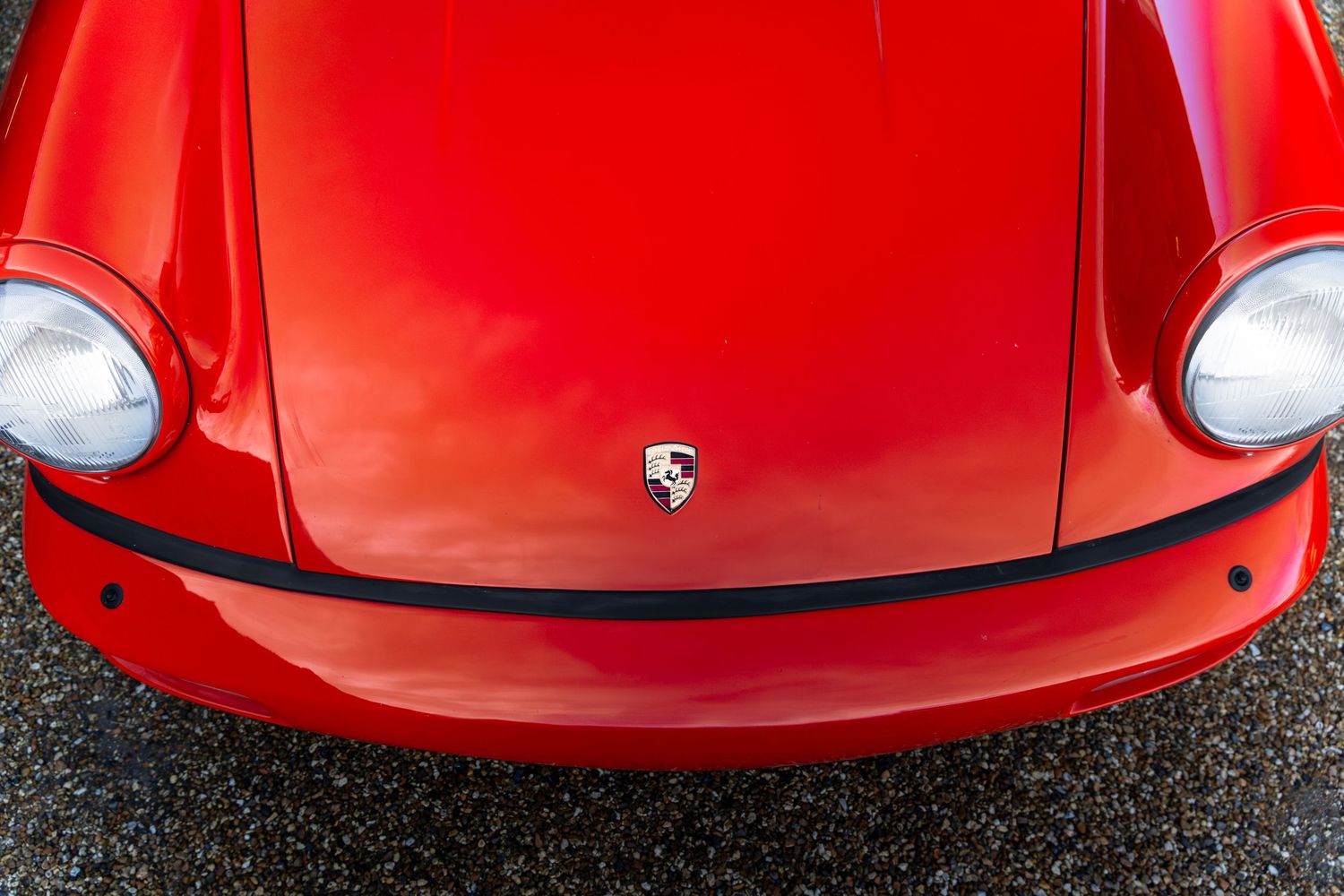 Close-up of a red Porsche 911 front hood featuring the iconic Porsche crest emblem and round headlights.