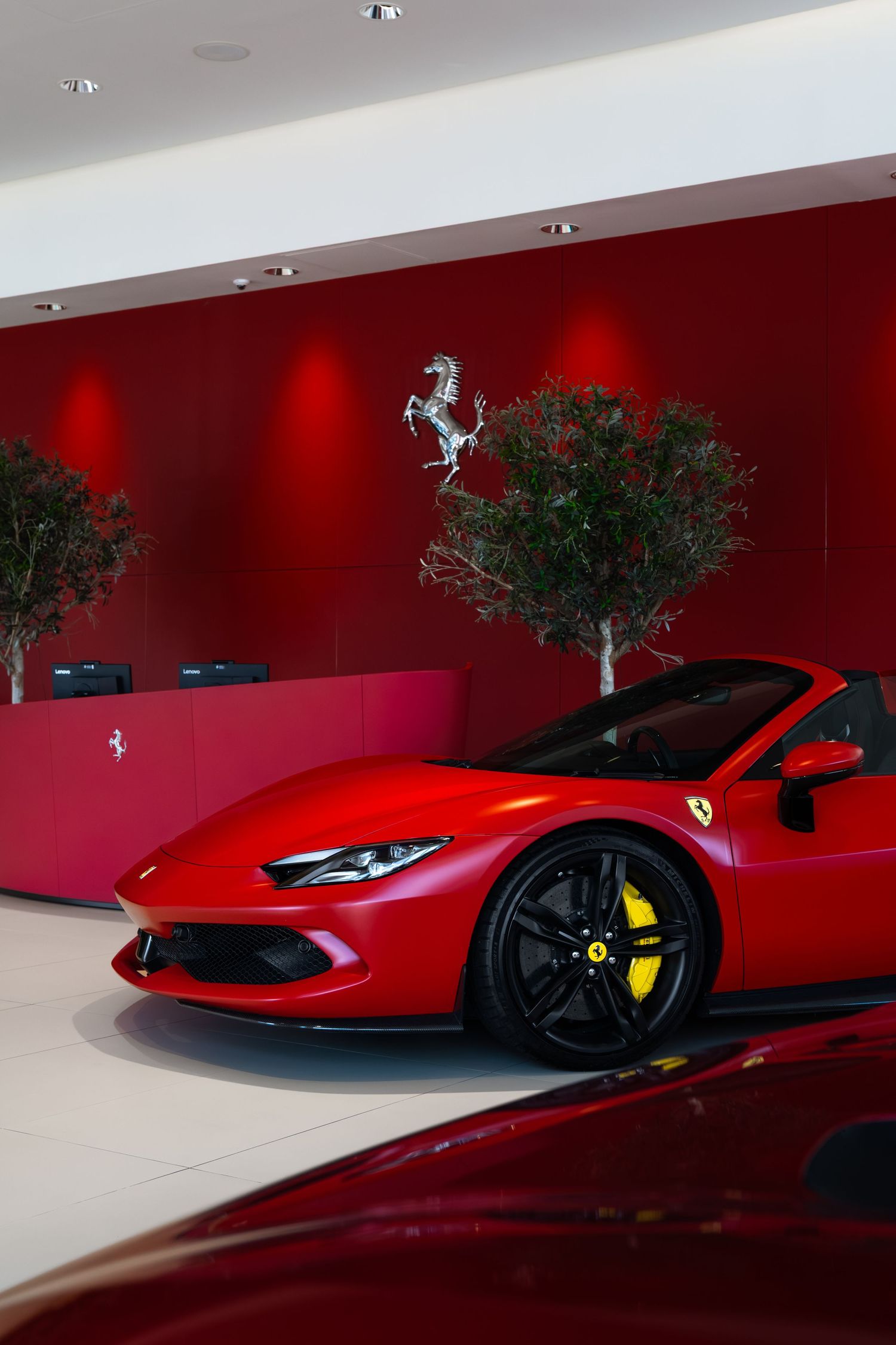 Red Ferrari sports car displayed in a luxury dealership showroom with the iconic prancing horse logo on the wall.