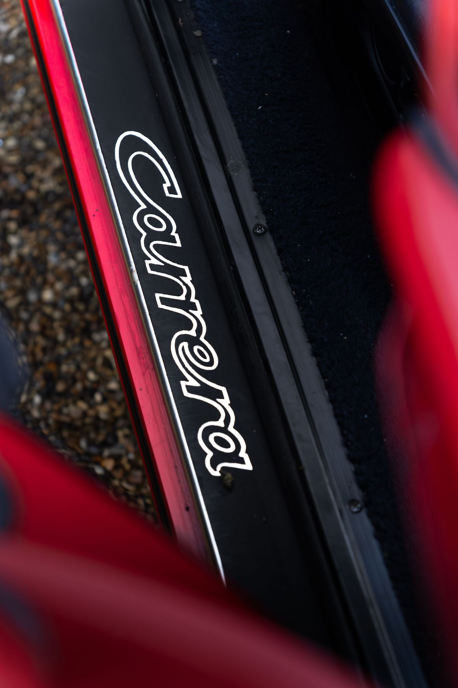 Close-up of Porsche 911 Carrera door sill plate with cursive Carrera script on black background.