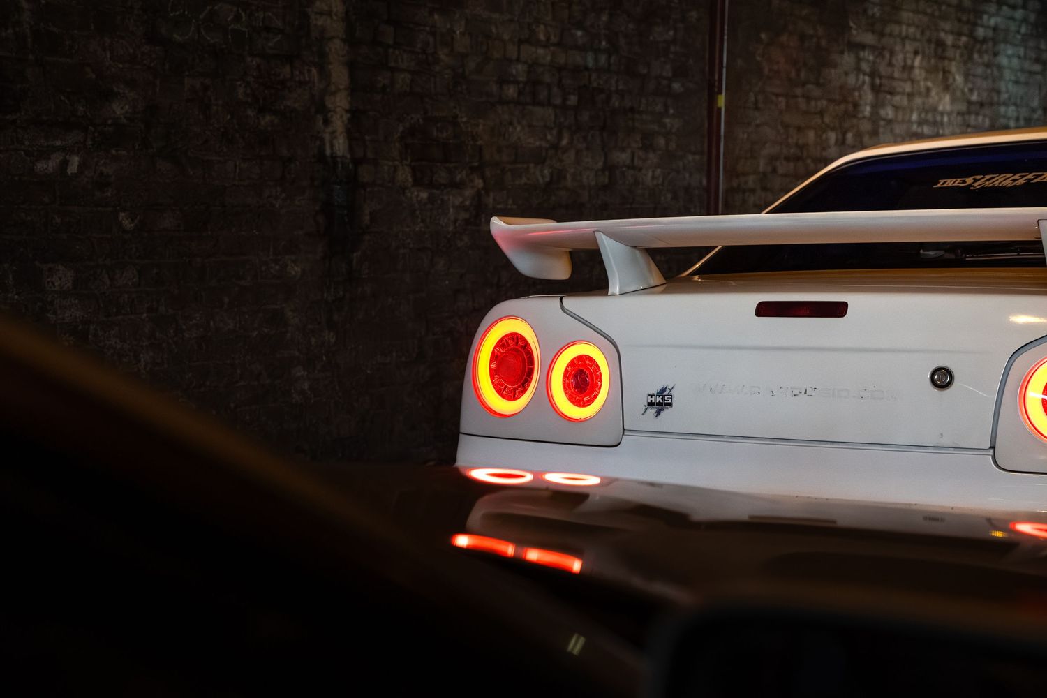 Rear view of white Nissan Skyline GT-R with large spoiler and glowing tail lights.