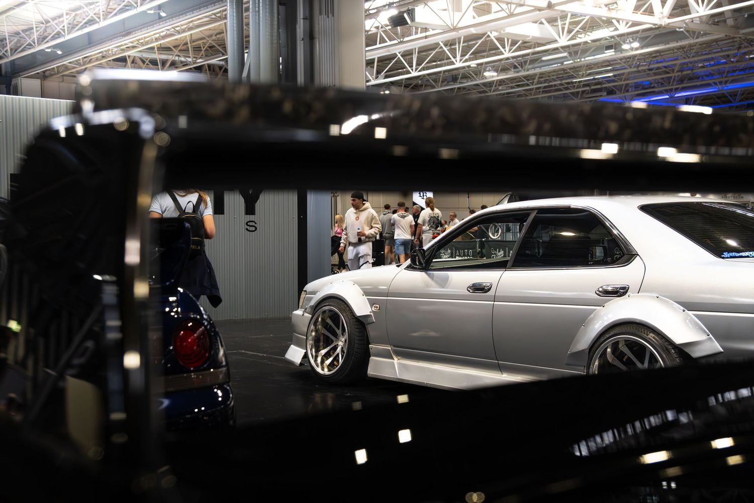 Silver modified sedan on display at an indoor automotive exhibition event.