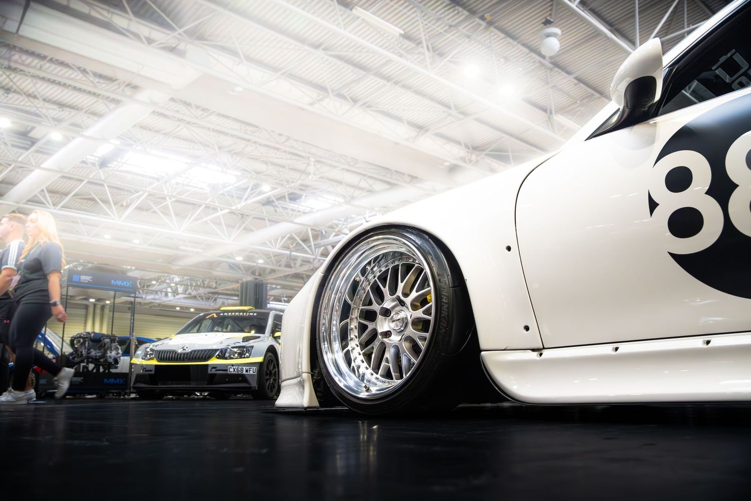 Low stance white race car number 88 with BBS wheels on display at indoor car show.