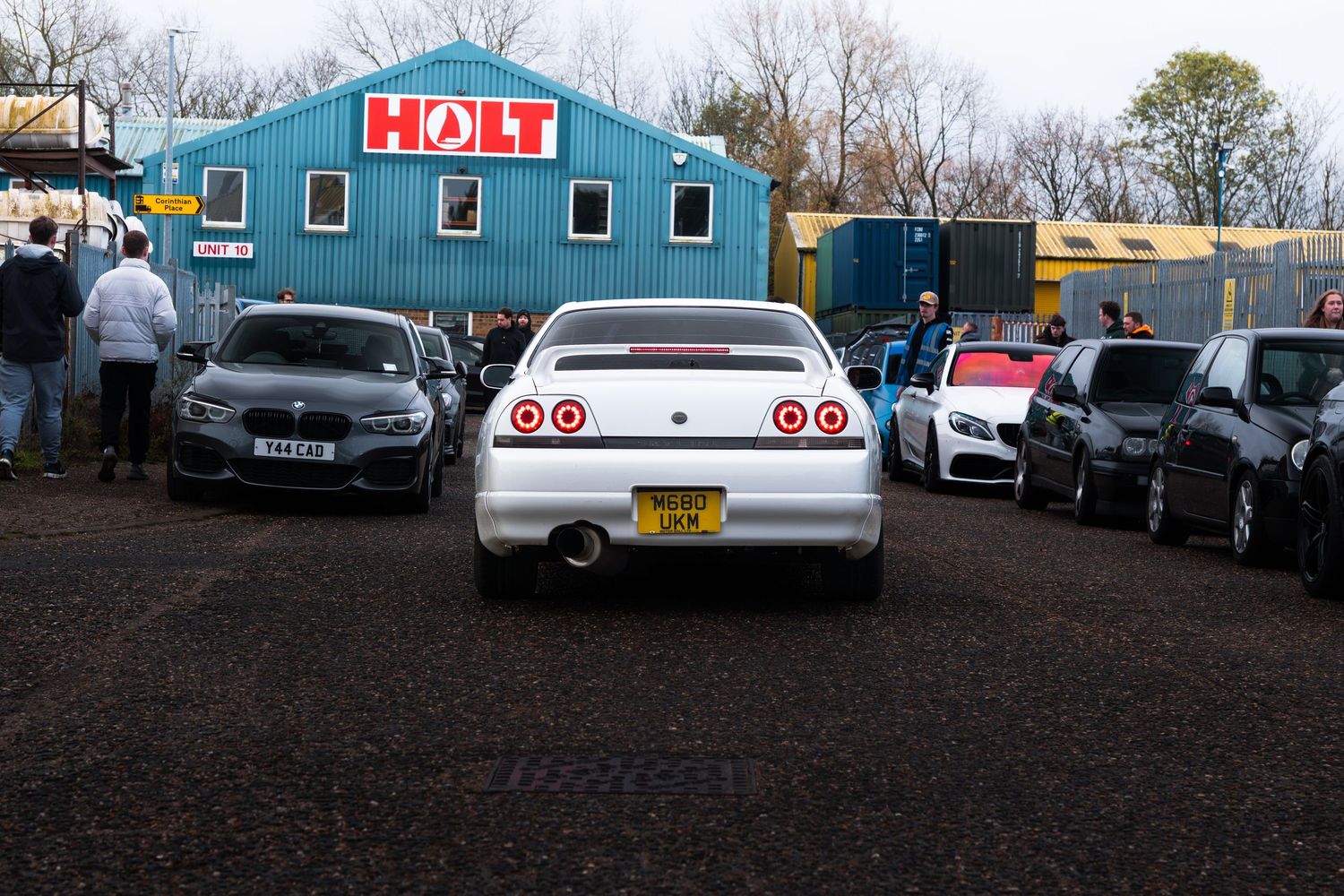 Rear view of a white Nissan Skyline R33 GT-R with yellow number plate at a car meet near Holt building.