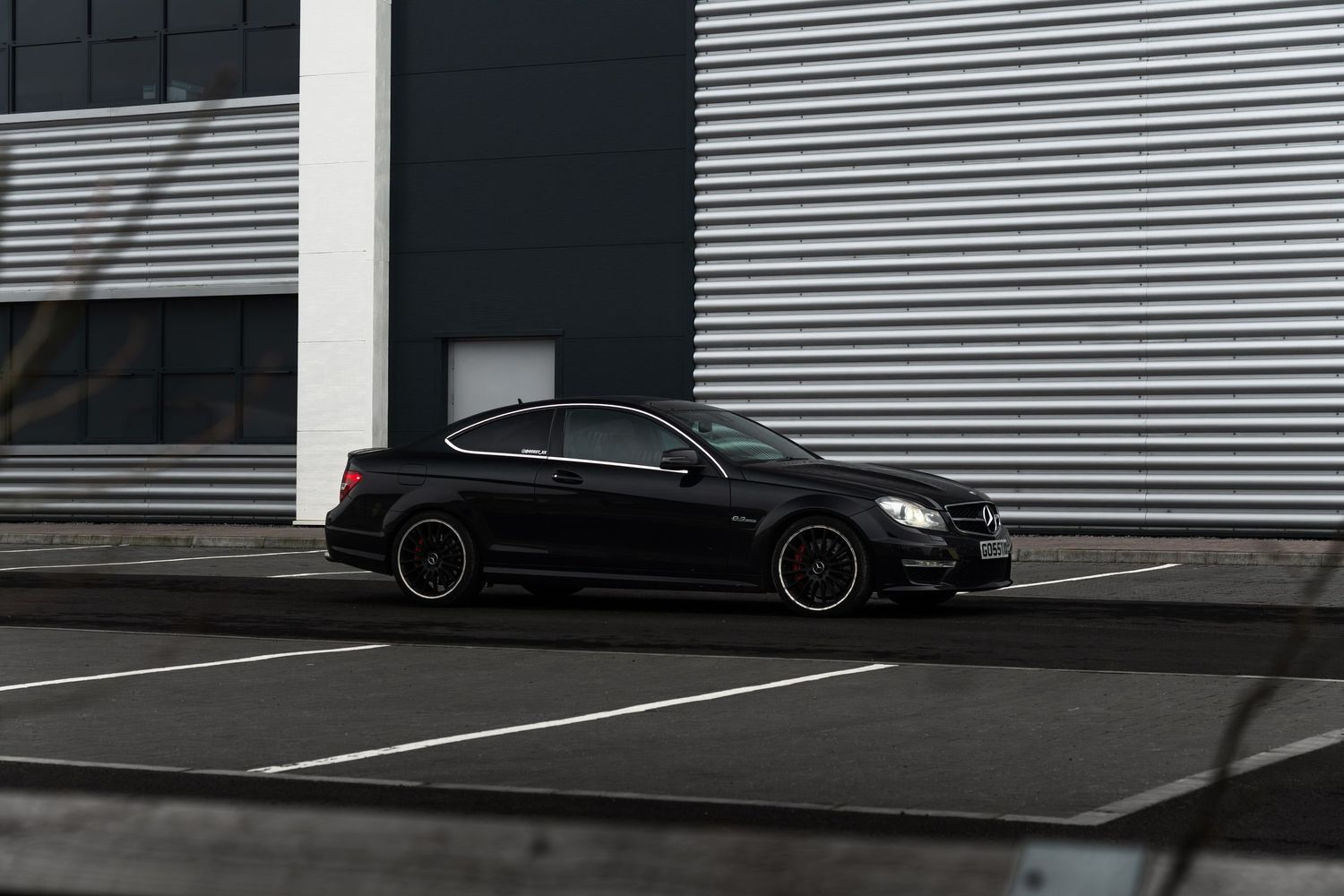 Black Mercedes-AMG C63 coupe in side profile view parked outside a modern industrial building.