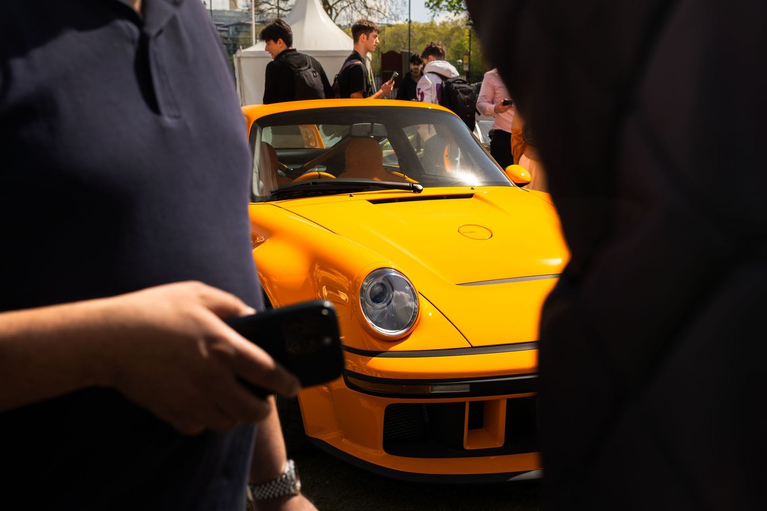 Bright yellow Porsche 911 RWB supercar surrounded by spectators at an outdoor automotive event.