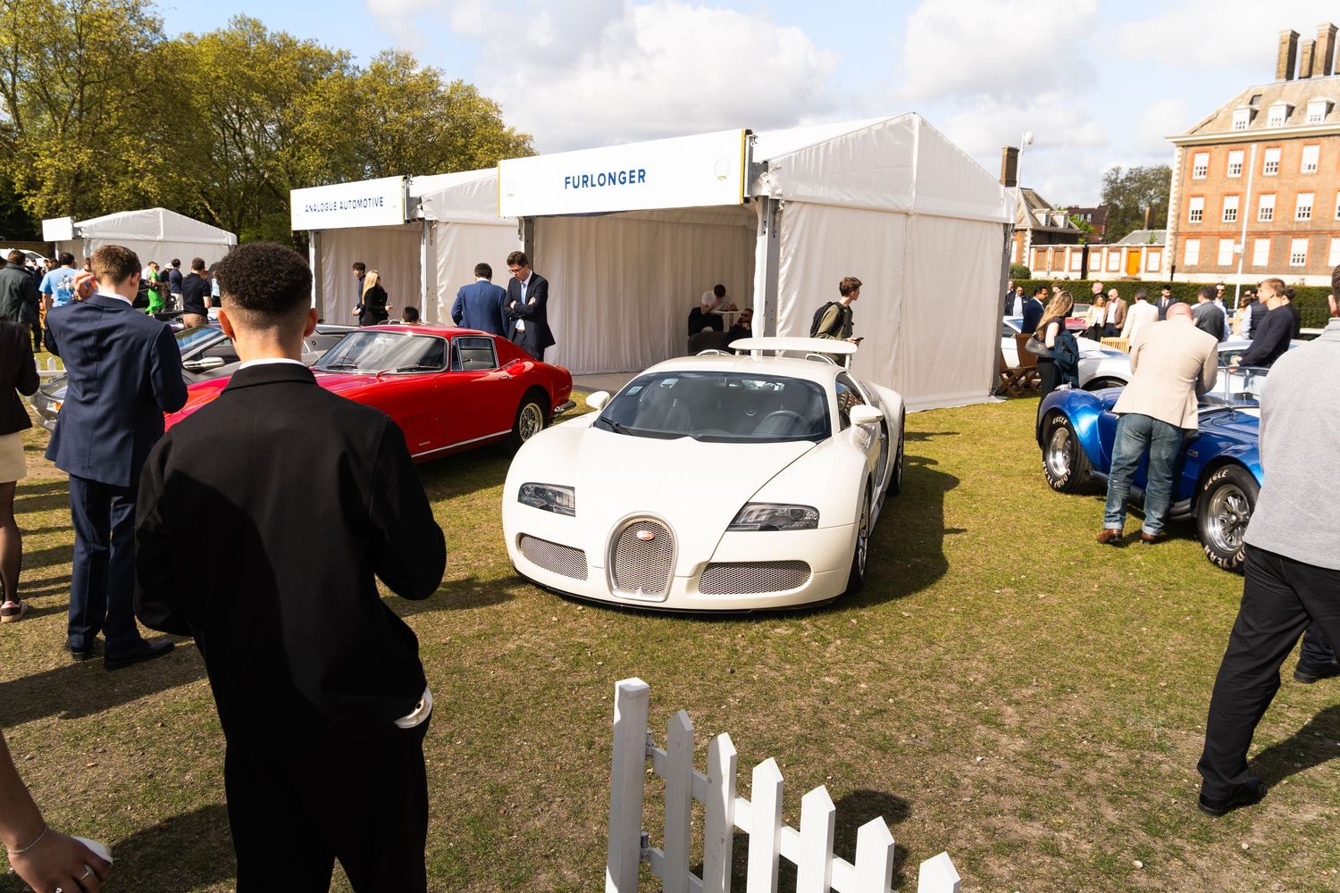 White Bugatti Veyron on display at an outdoor luxury car show near a white marquee tent.